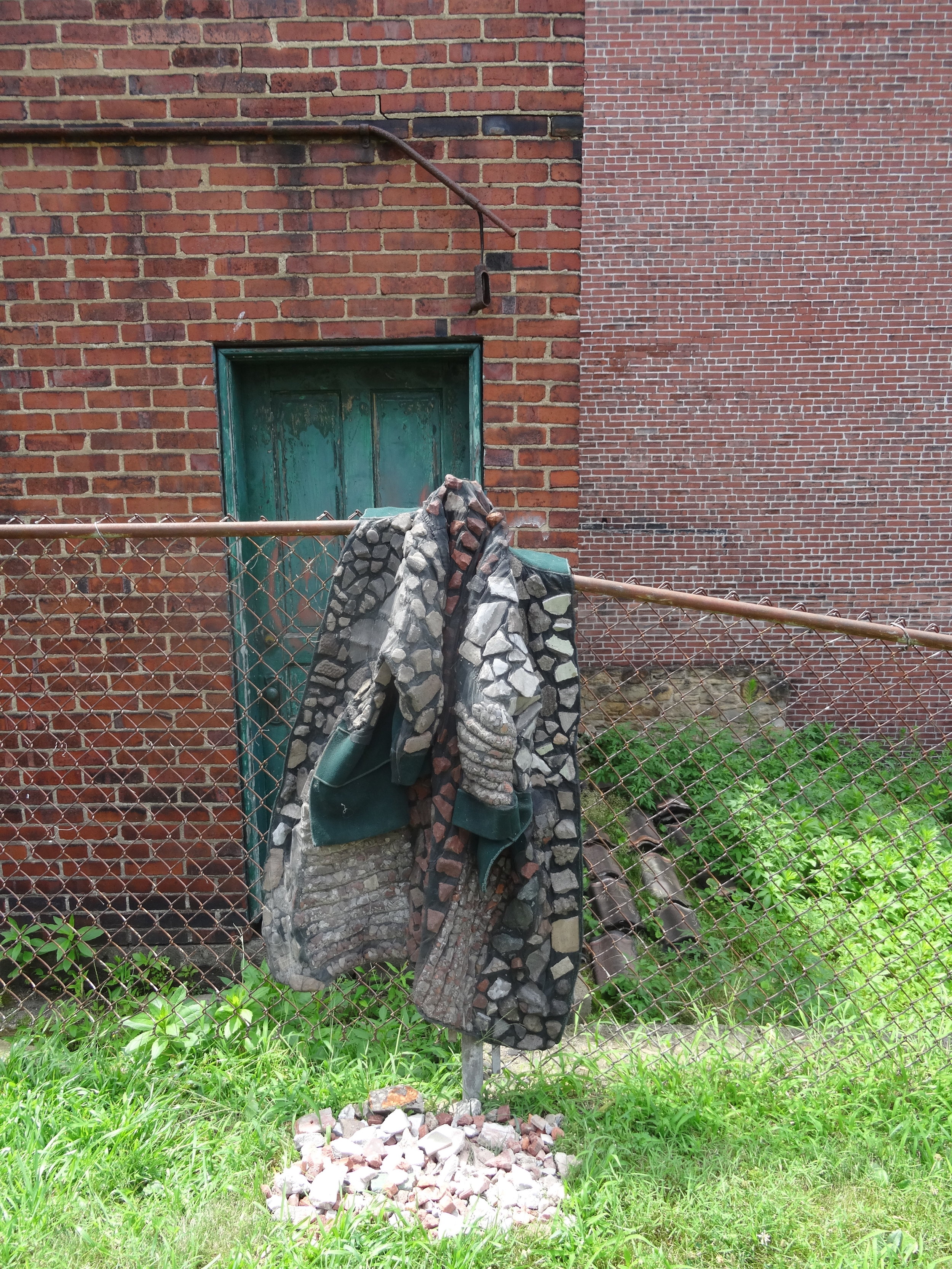  9. wearing your debts wool felt coat, found construction debris, steel window screen, thread. 40” x 36” Location: Upper garden to the right, along metal fence, hanging on fence post. 