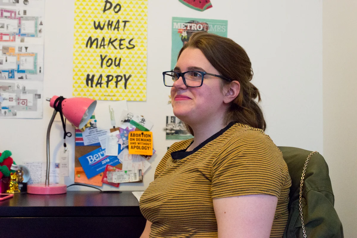 Haggerty sits at her desk, in front of pinned signs and notes like a Bernie Sanders sticker and an "ABORTION ON DEMAND AND WITHOUT APOLOGY!" sign that display her leftist leanings.