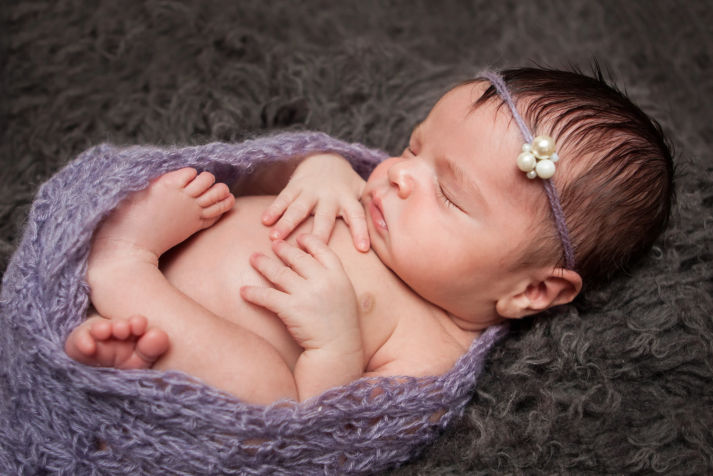 Newborn baby girl wrapped in purple knit with pearl headband tieback on grey rug, Westchester County, NY Newborn Photographer Amanda Noelle Photography.