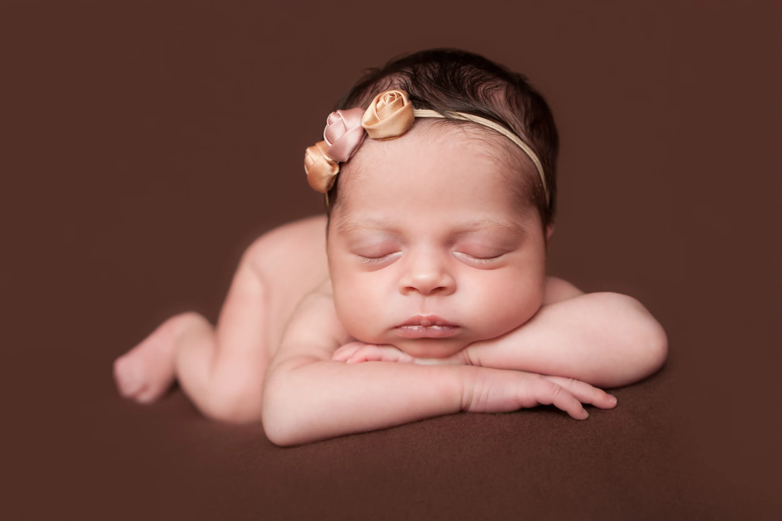 Newborn baby girl, shabby rosebud flower headband orange pink nude, brown backdrop fabric blanket, head chin on hands pose, sleeping baby pose on beanbag, Westchester County, New Rochelle, White Plains, Pelham, New York Newborn Photographer, Amanda Noelle Photography