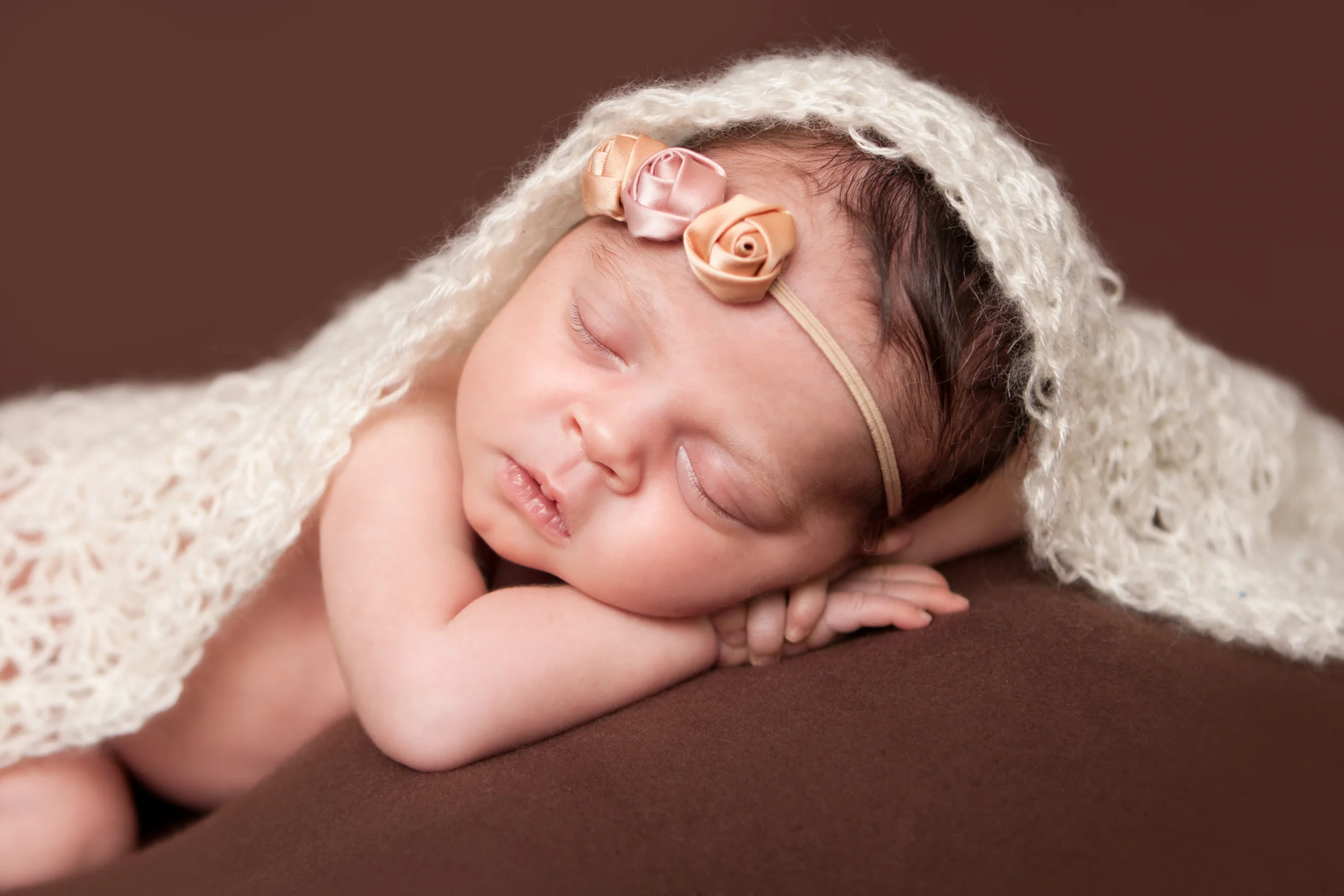 Newborn baby girl, shabby rosebud flower headband orange pink nude, brown backdrop fabric blanket, white creme crochet wrap, head on hands pose, sleeping baby pose on beanbag, Westchester County, New Rochelle, White Plains, Pelham, New York Newborn Photographer, Amanda Noelle Photography