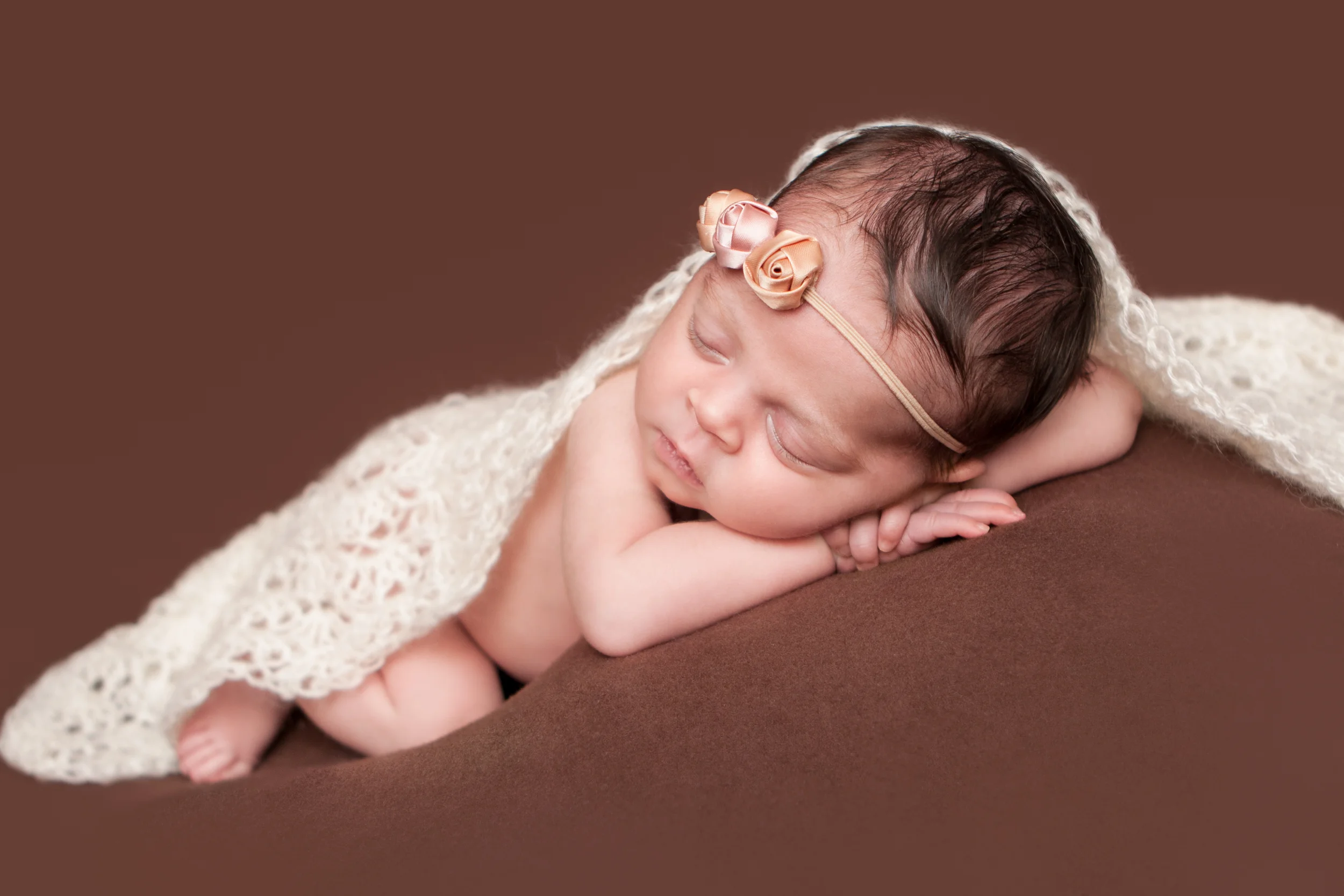Newborn baby girl, shabby rosebud flower headband orange pink nude, brown backdrop fabric blanket, white creme crochet wrap, head on hands pose, sleeping baby pose on beanbag, Westchester County, New Rochelle, White Plains, Pelham, New York Newborn Photographer, Amanda Noelle Photography