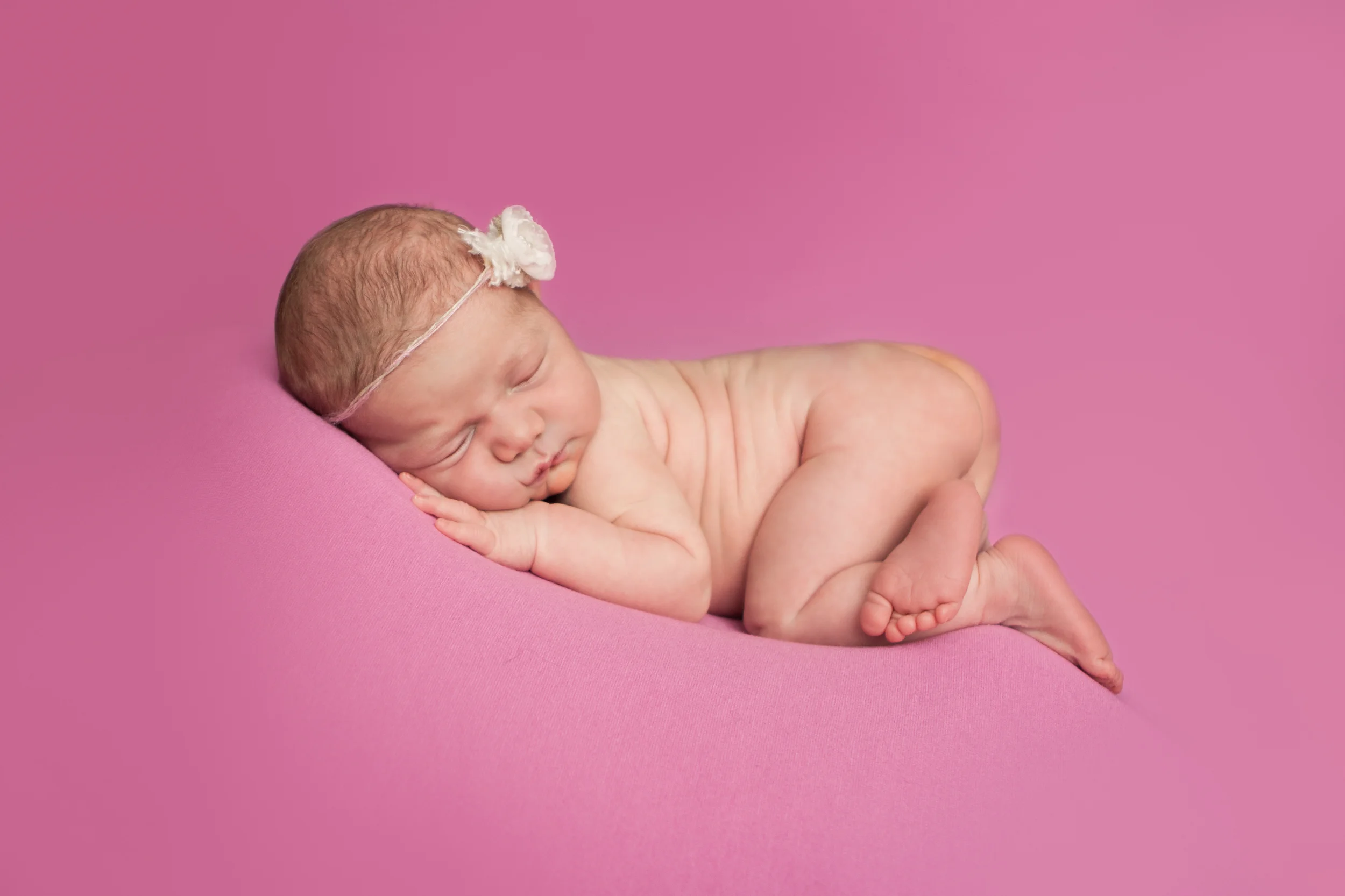 Newborn baby girl with flower delicate tieback headband, bean bag pose on pink fabric backdrop, Westchester County, New York Newborn Photographer, Amanda Noelle Photography.