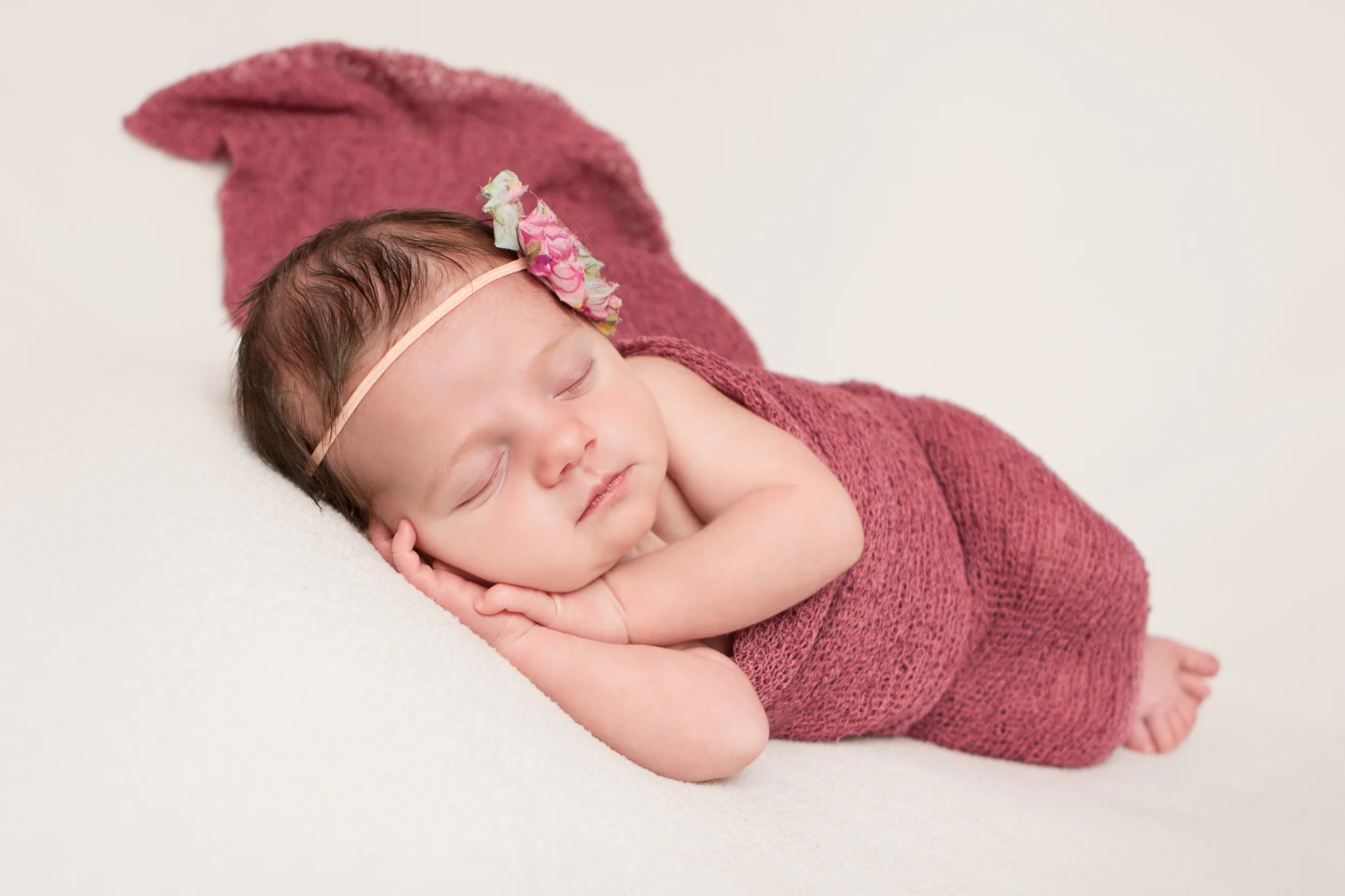 Newborn baby girl with pink mint creme shabby chic flower headband, pink berry maroon stretch wrap, on white fabric blanket backdrop, beanbag pose, Westchester County, New York Newborn Photographer, Amanda Noelle Photography.