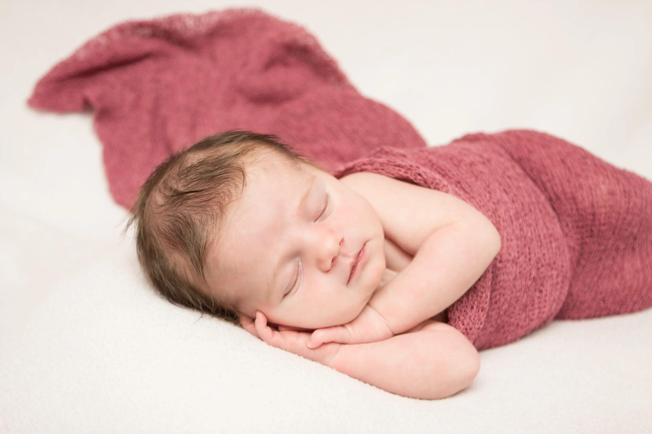 Newborn baby girl, pink berry maroon stretch wrap, on white fabric blanket backdrop, beanbag pose, Westchester County, New York Newborn Photographer, Amanda Noelle Photography.