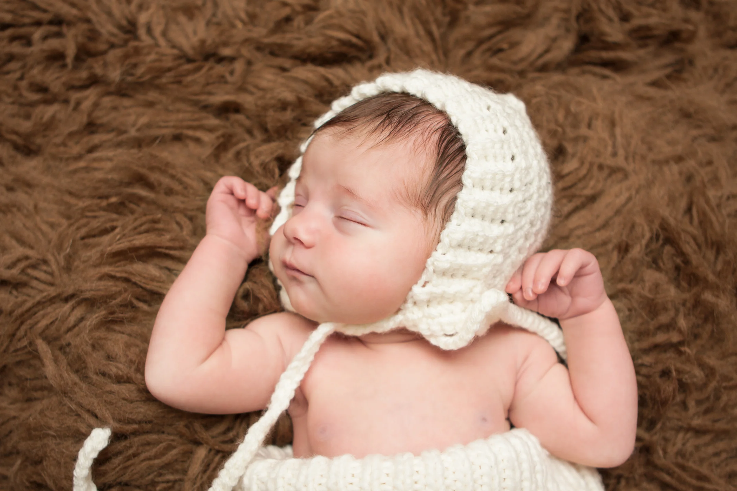 Newborn baby girl , creme white crochet bonnet in, in creme white crochet knit wrap sack on brown flokati rug, Westchester County, New York Newborn Photographer, Amanda Noelle Photography.