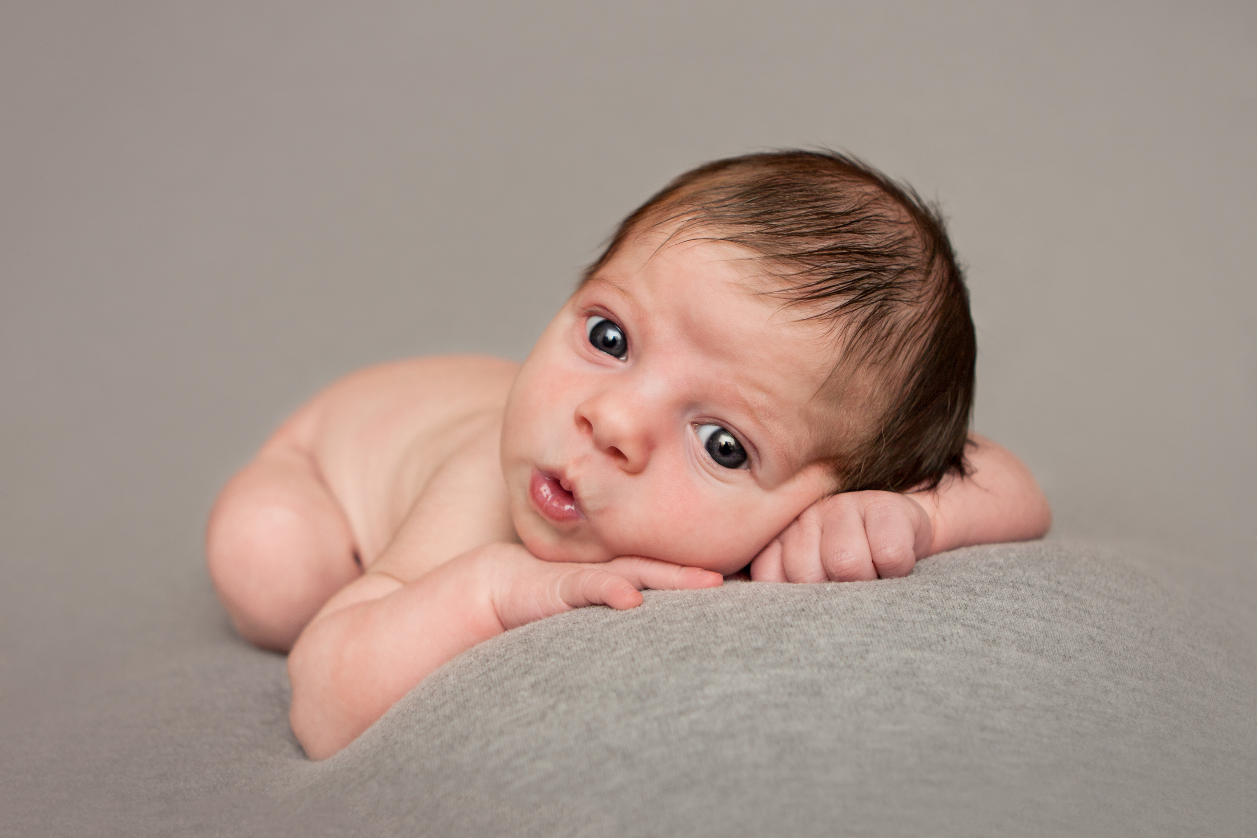 Newborn baby girl awake with blue eyes, on grey fabric blanket backdrop, head on hands beanbag pose, Westchester County, New York Newborn Photographer, Amanda Noelle Photography.