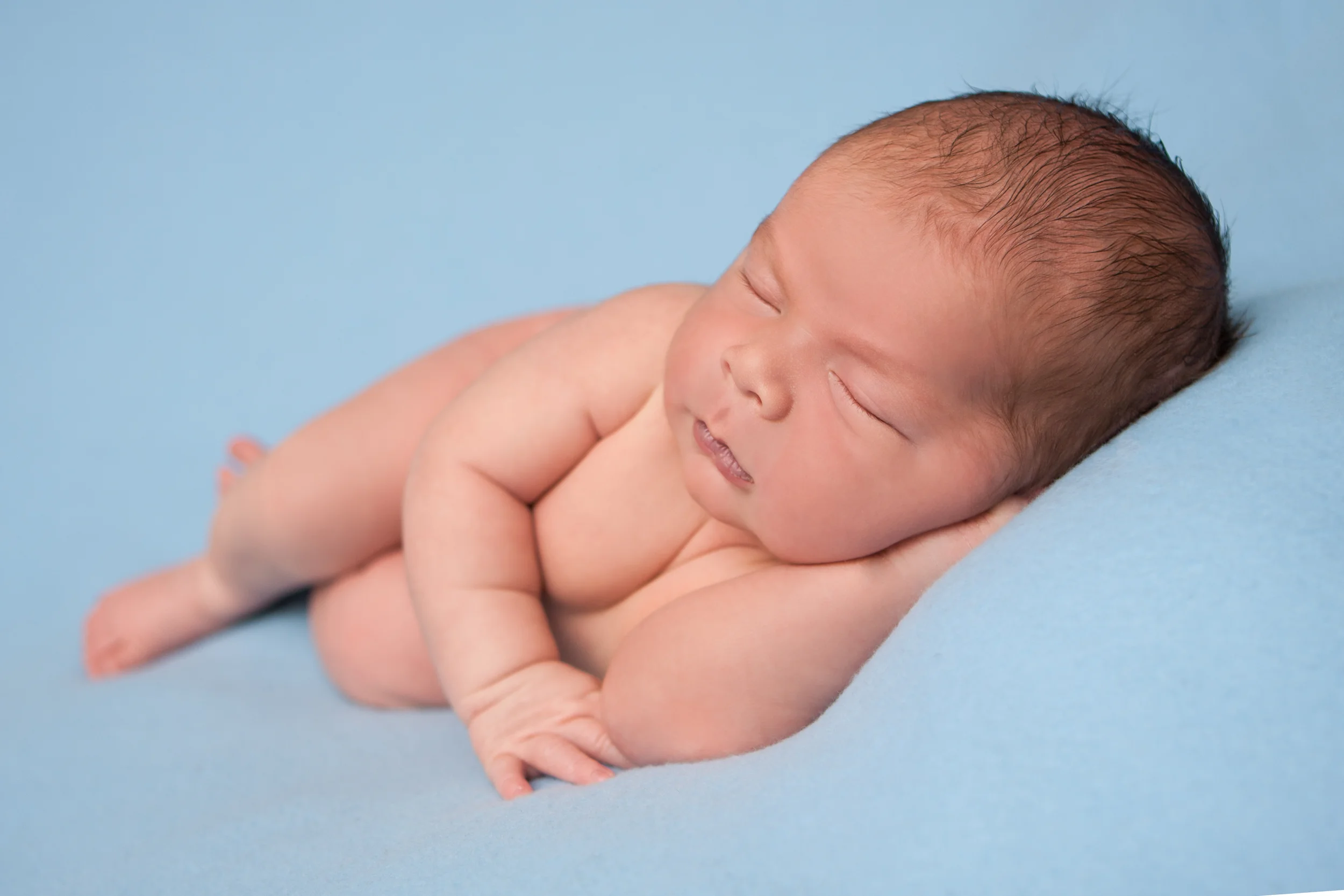 Newborn baby boy chubby sleeping on blue fabric blanket backdrop, bean bag pose Westchester County, New York newborn photographer, Amanda Noelle Photography.