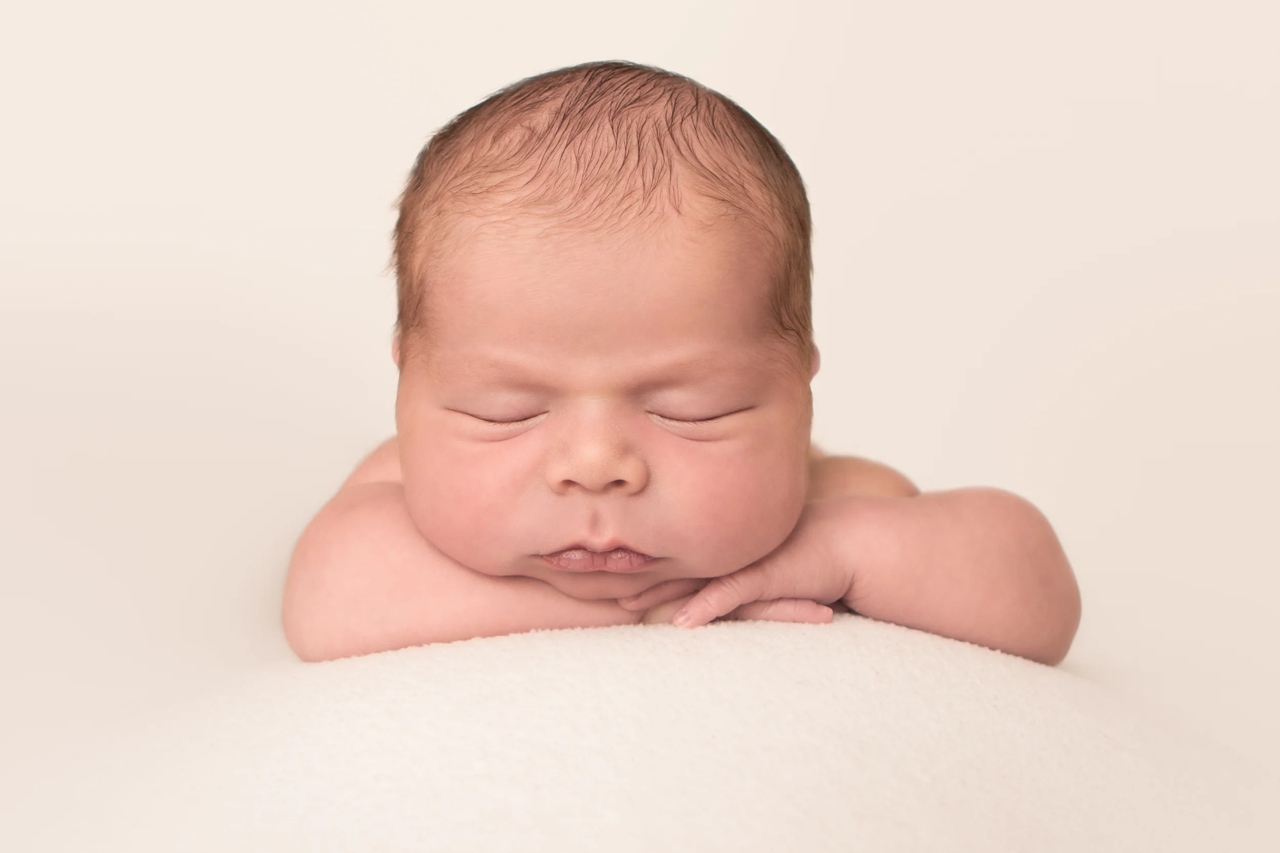 Newborn baby boy chubby, on cream creme white fabric blanket backdrop, head on hands wrists bean bag pose, Westchester County, New York newborn photographer, Amanda Noelle Photography.