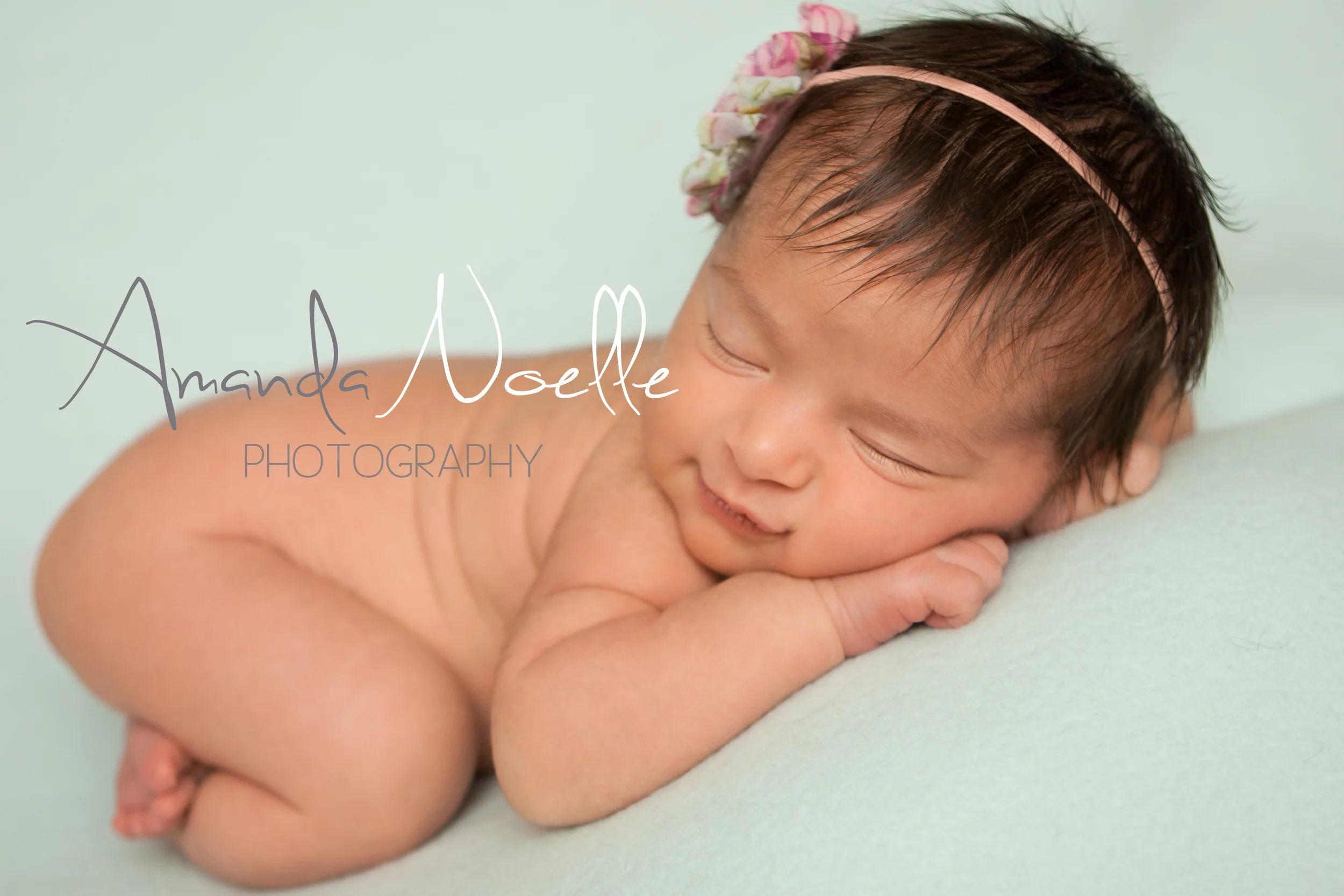 Newborn baby girl sleeping smile with shabby chic pink headband on teal mint aqua fabric backdrop, tushy up beanbag pose, Westchester, County New York Newborn Photographer, Amanda Noelle Photography.