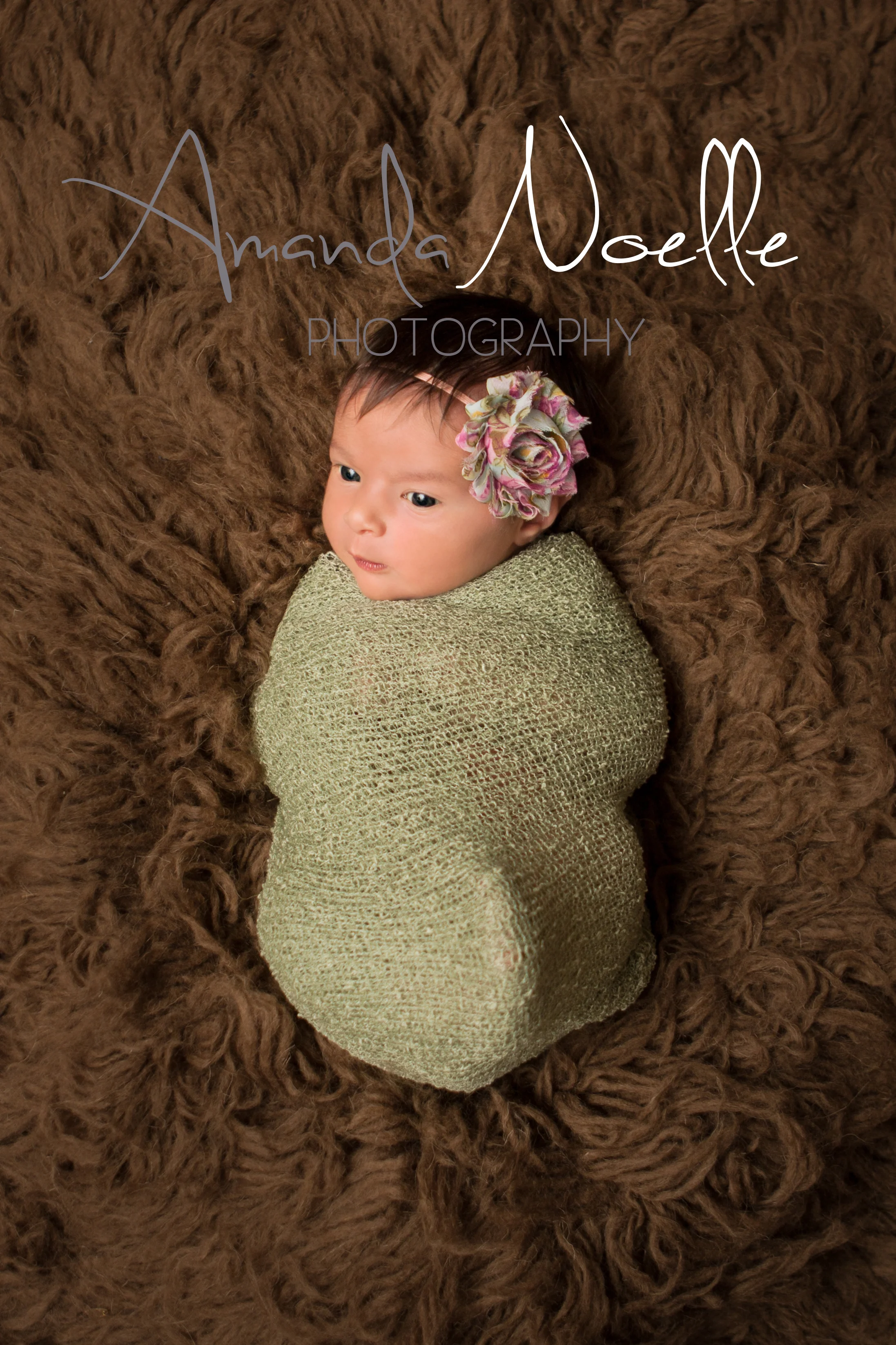 Newborn baby girl awake with pink and green shabby chic flower headband wrapped in stretch knit green wrap on brown flokati rug, Westchester, County New York Newborn Photographer, Amanda Noelle Photography.