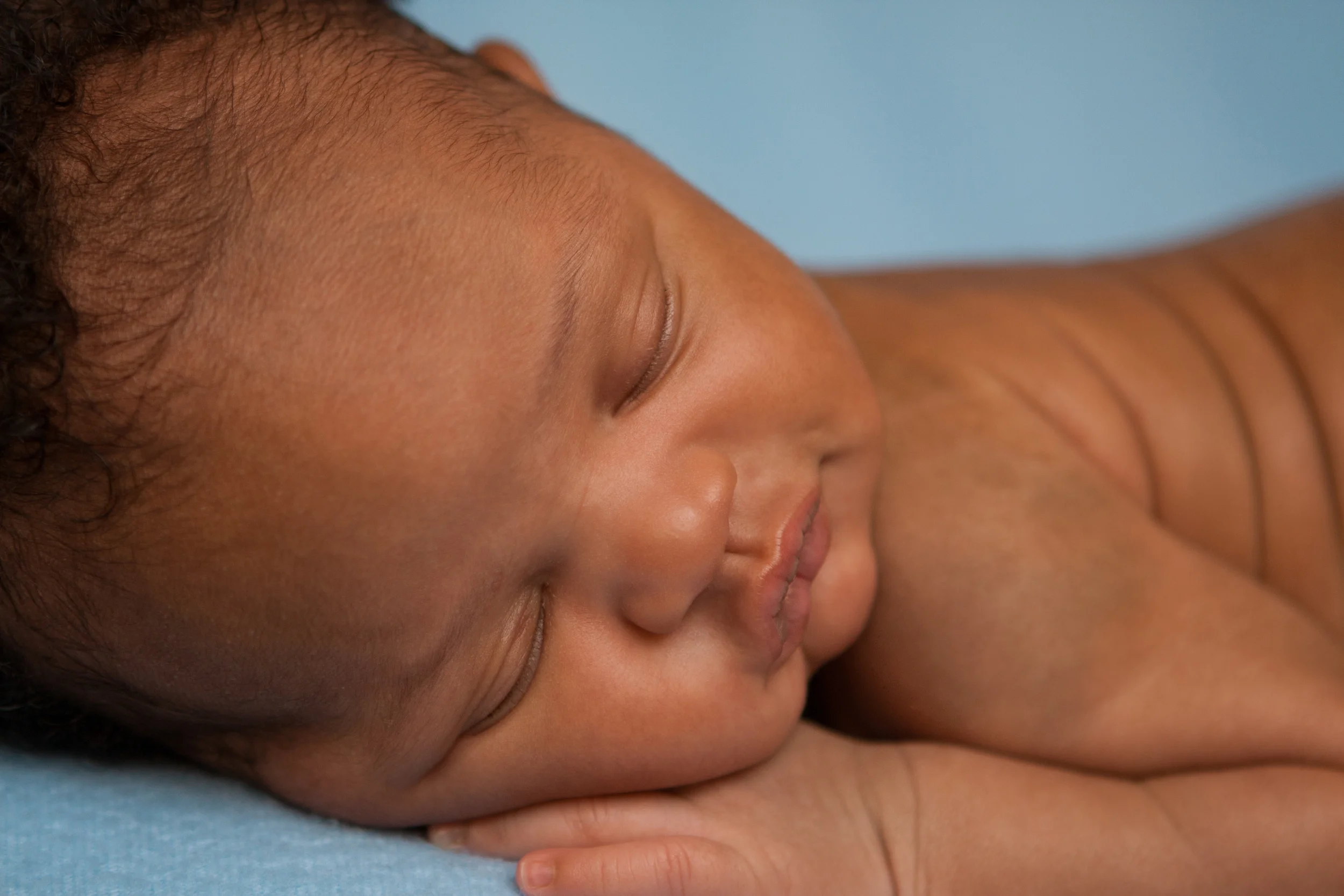 Newborn baby boy j black curly hair, african american, sleeping bean bag pose, blue fabric blanket backdrop, Westchester County, New York Newborn Photographer, Amanda Noelle Photography.