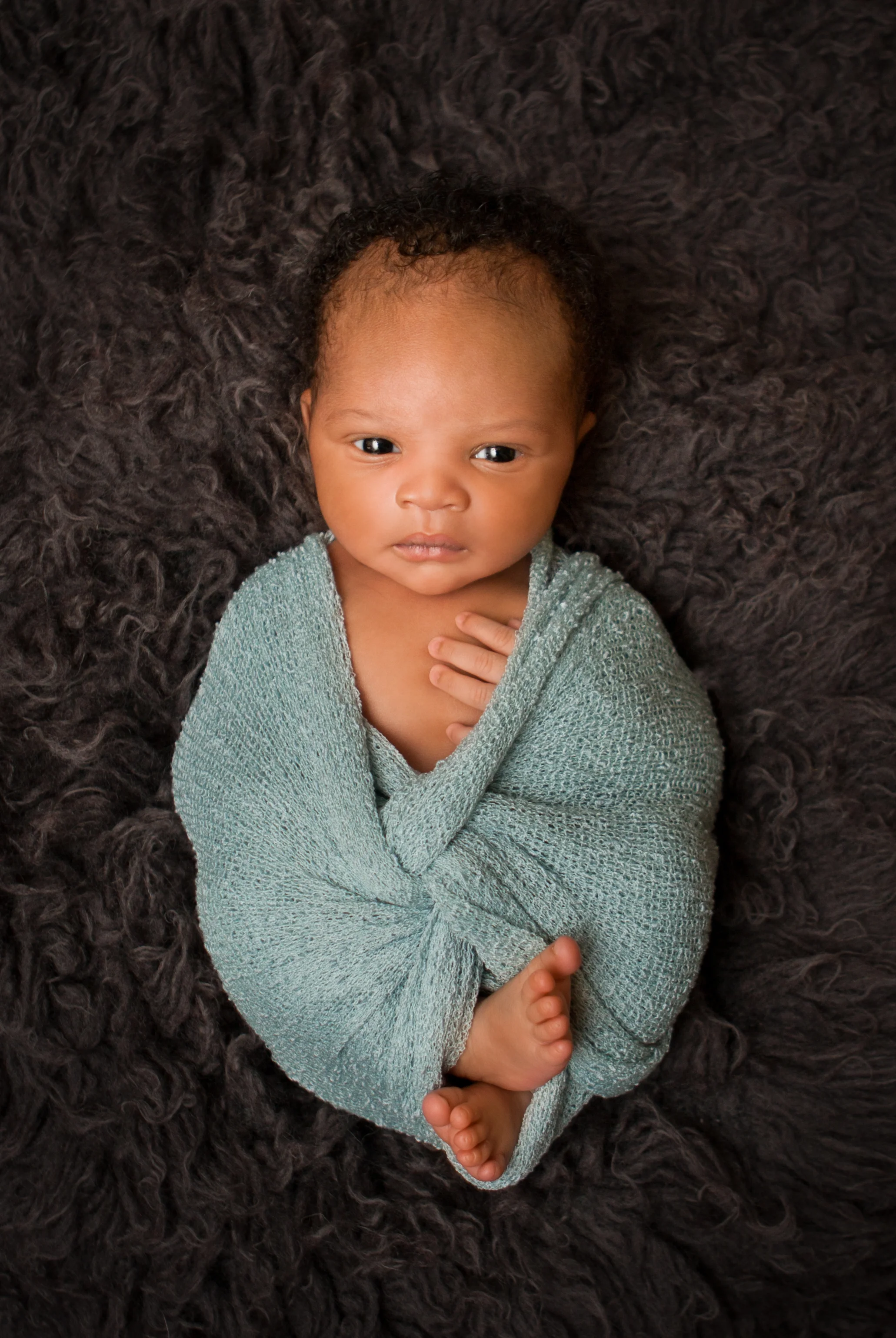 waNewborn baby boy j awake black curly hair wrapped in grey gray blue stretch knit wrap, african american, sleeping on grey gray blue flokati rug , Westchester County, New York Newborn Photographer, Amanda Noelle Photography.