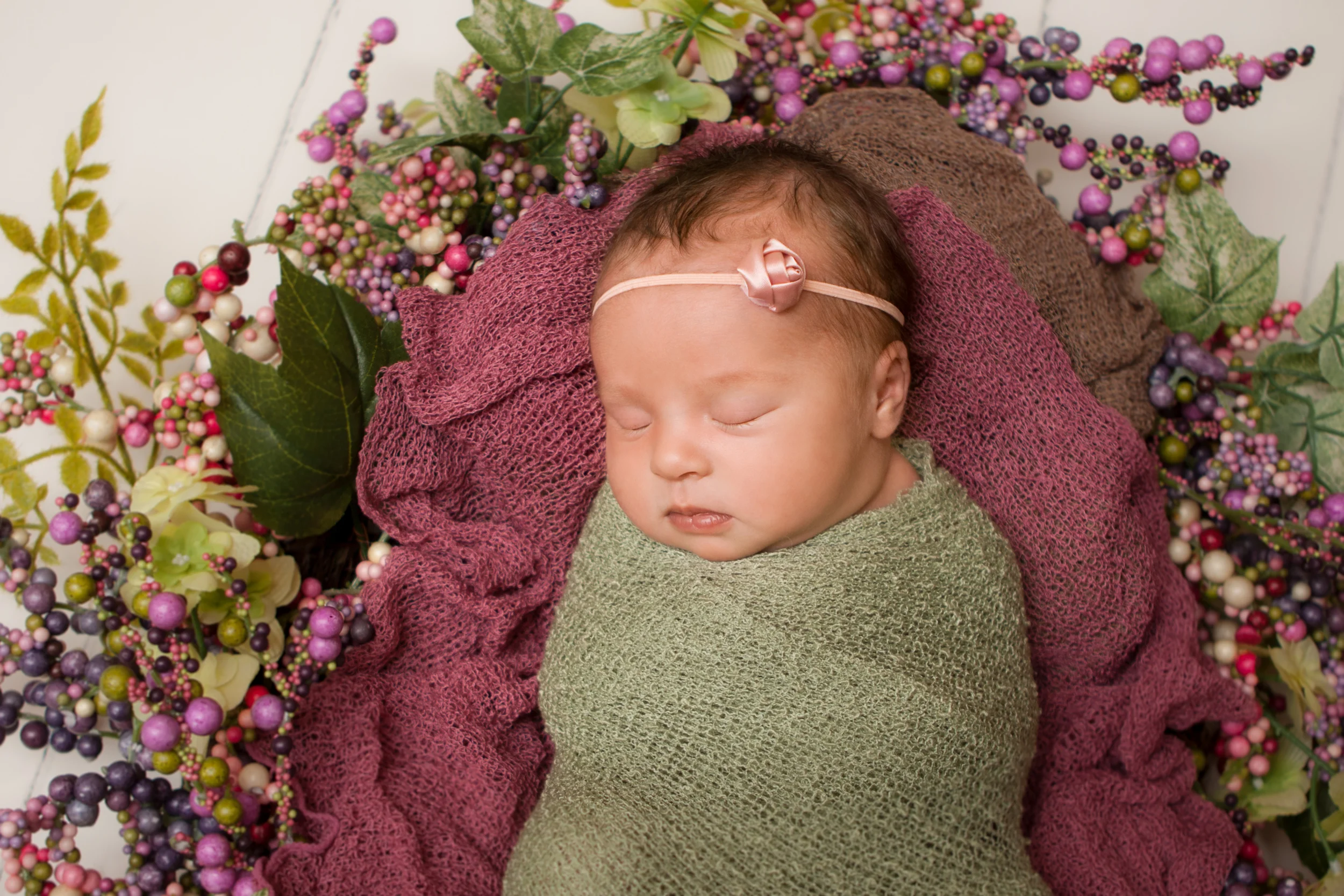 Newborn baby girl sleeping spring photos, wrapped in green knit stretch wrap, spring wreath, white wood floor backdrop.