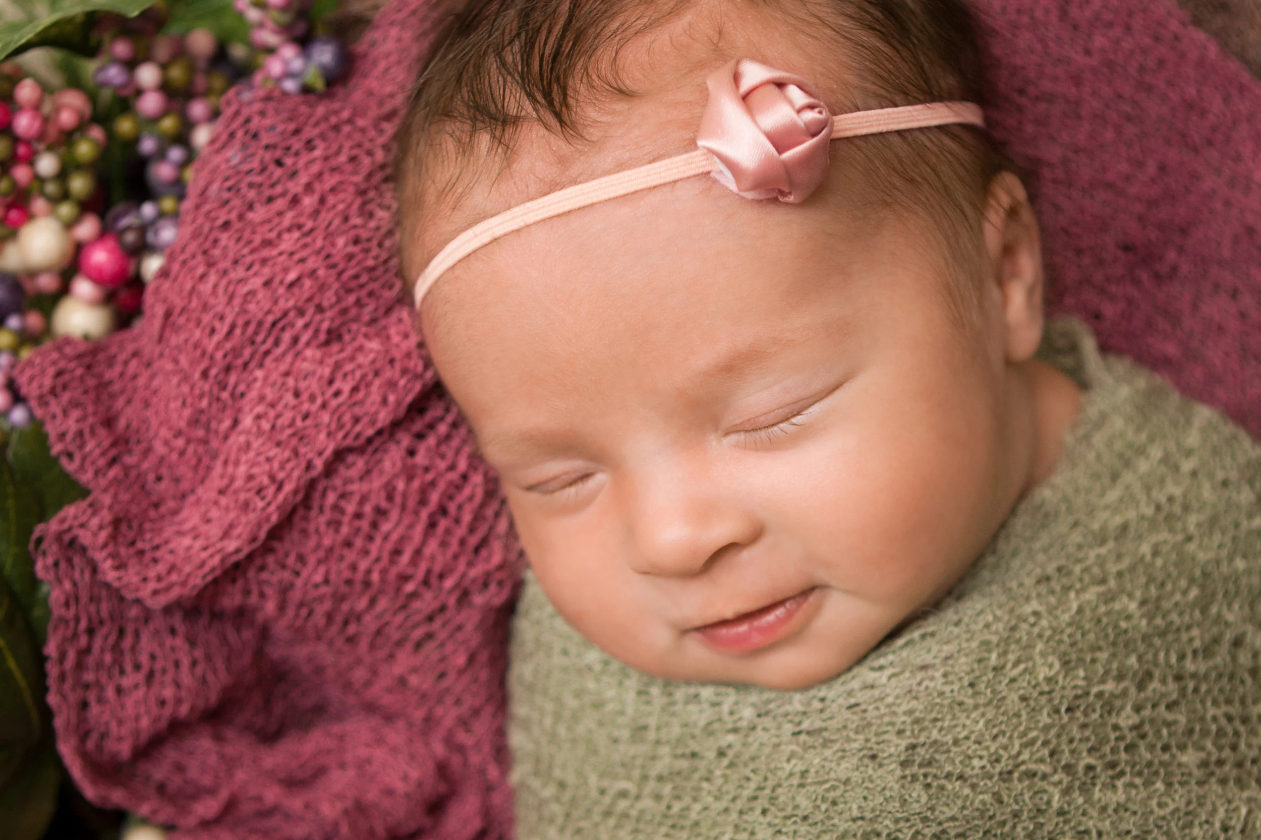Newborn baby girl sleeping smile spring photos, wrapped in green knit stretch wrap, spring wreath, white wood floor backdrop.
