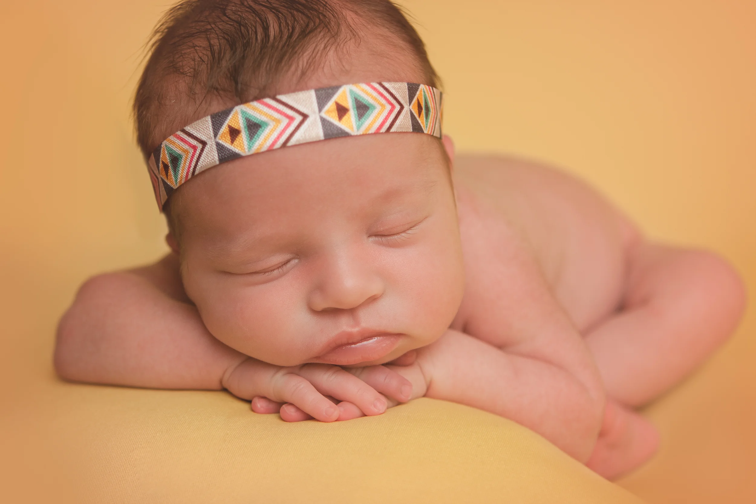 Newborn baby girl sleeping pose, bohemian headband, yellow blanket fabric backdrop, head chin on hands bean bag pose.