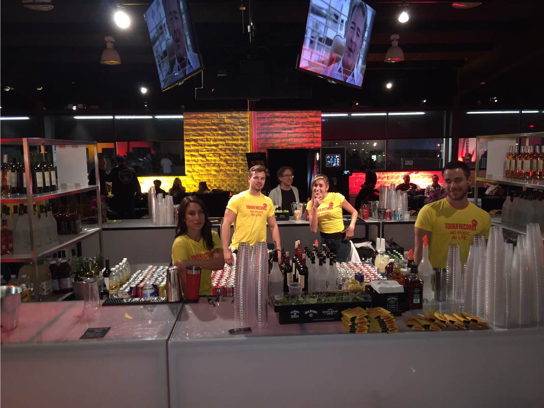 Platinum staff in matching event shirts behind a bar at a premiere party