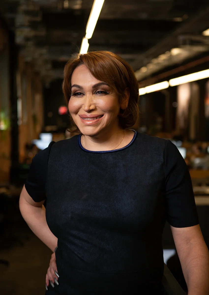 A transgender woman in business attire smiling in an office.jpg