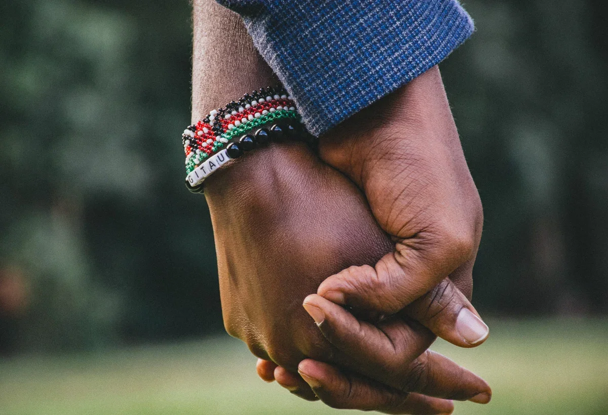 A close-up of two LGBTQ+ hands holding each other, with one hand wearing colorful beaded bracelets.
