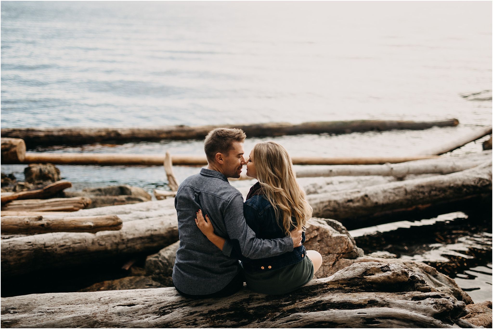couple sitting on log lighthouse park arms around each other