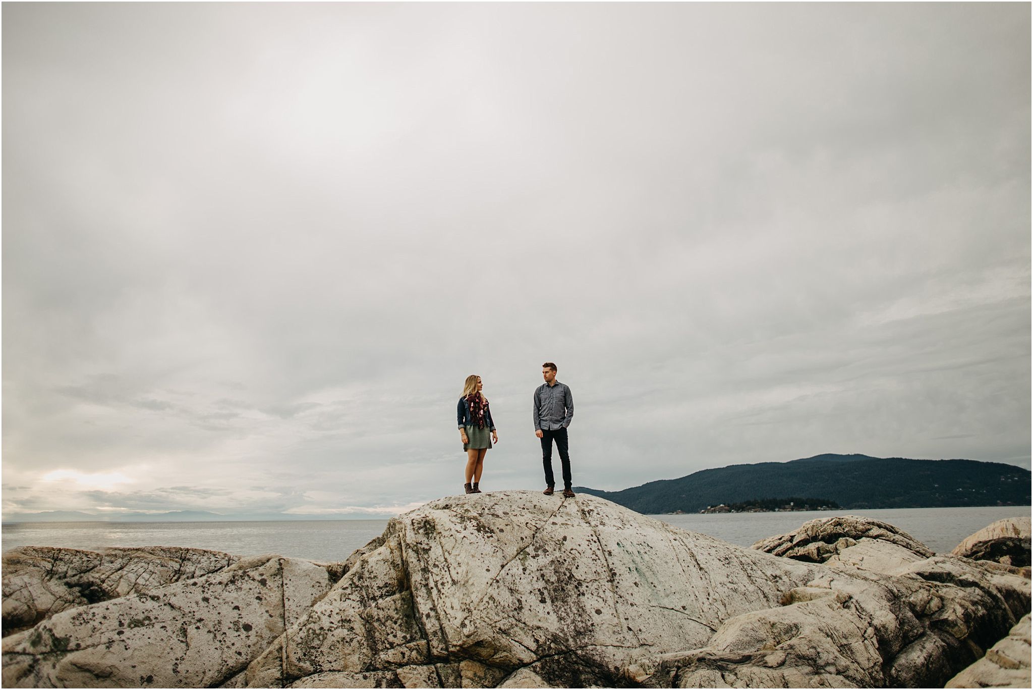 couple standing on top of rock by ocean at lighthouse park