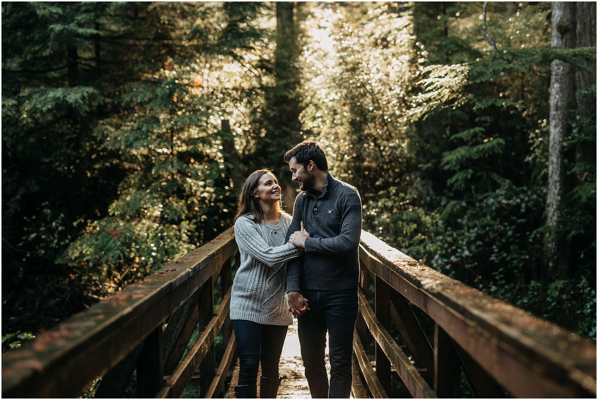 couple walking on bridge sun shining through trees rolley lake engagement