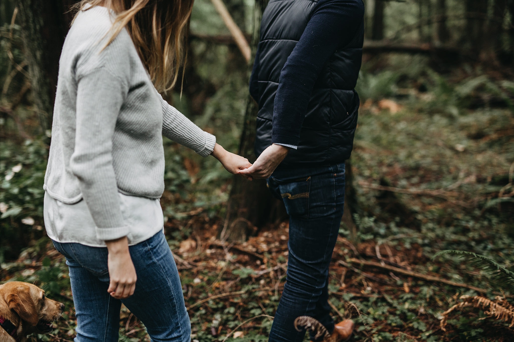 couple holding hands walking through forest pacific spirit park engagement
