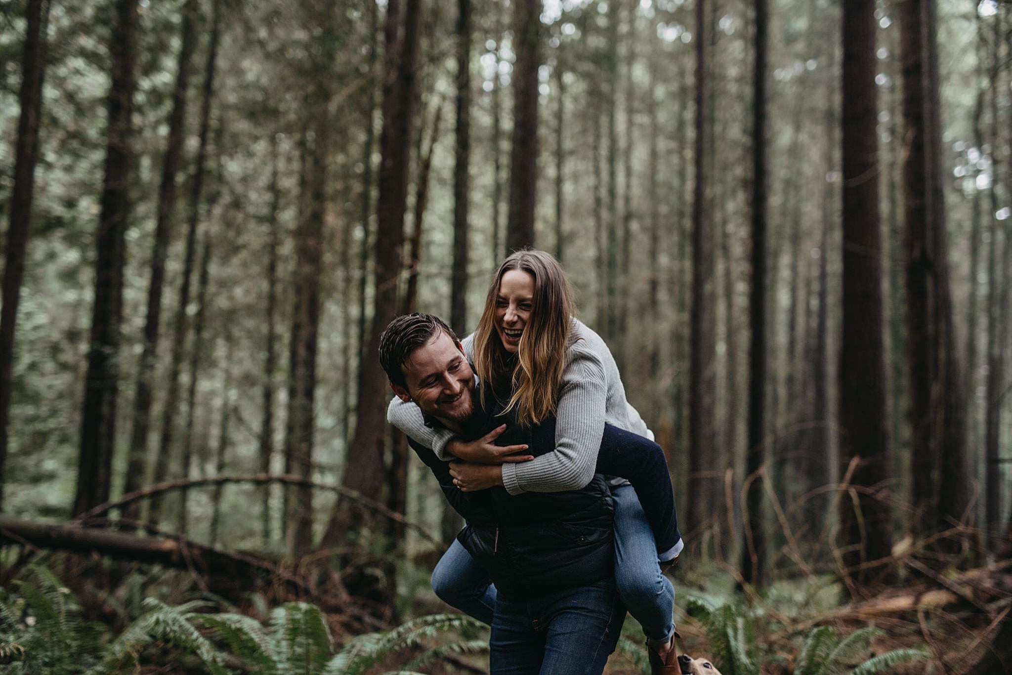 couple playful fun piggyback candid forest tall trees pacific spirit park