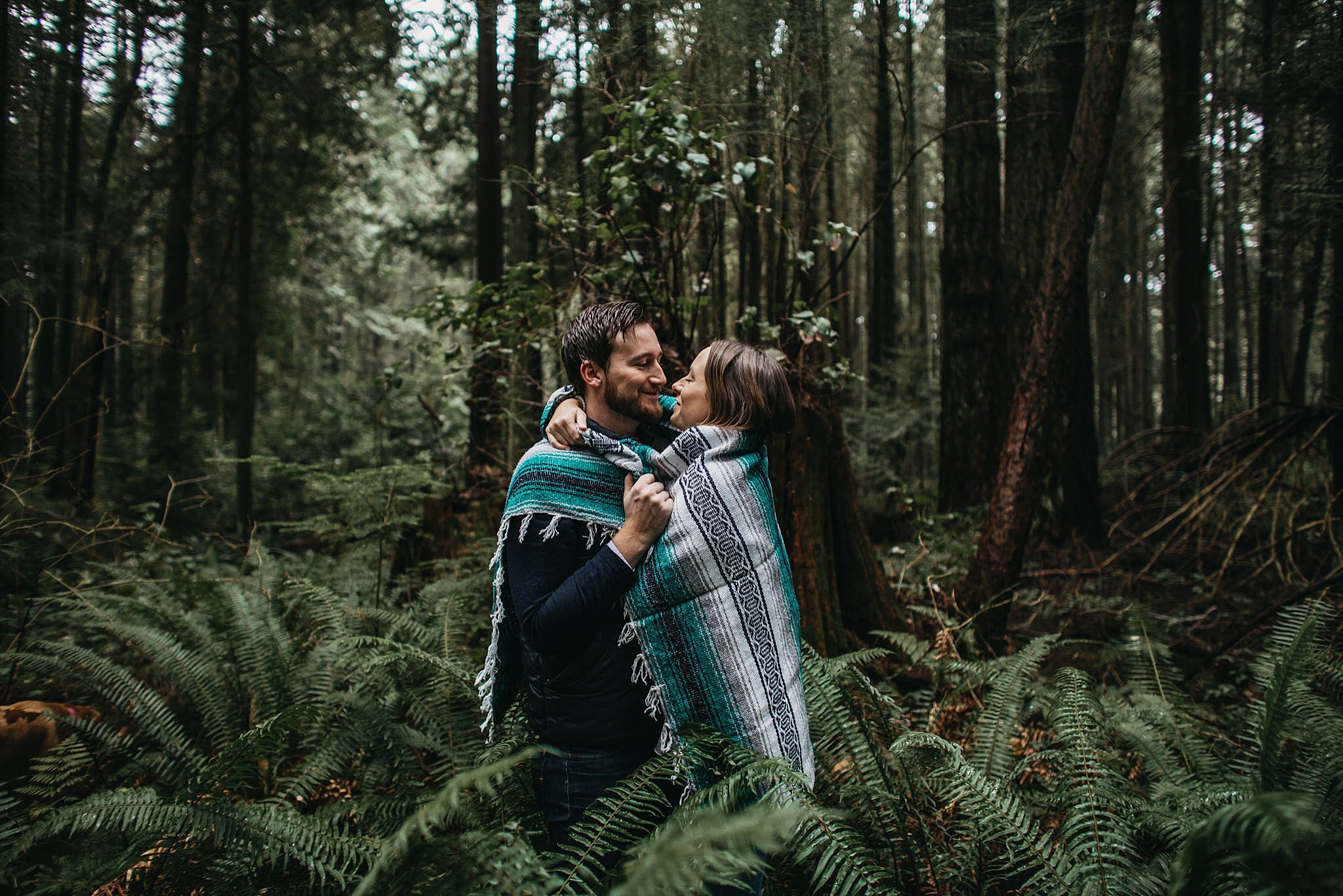 couple wrapped in blanket in forest pacific spirit park engagement