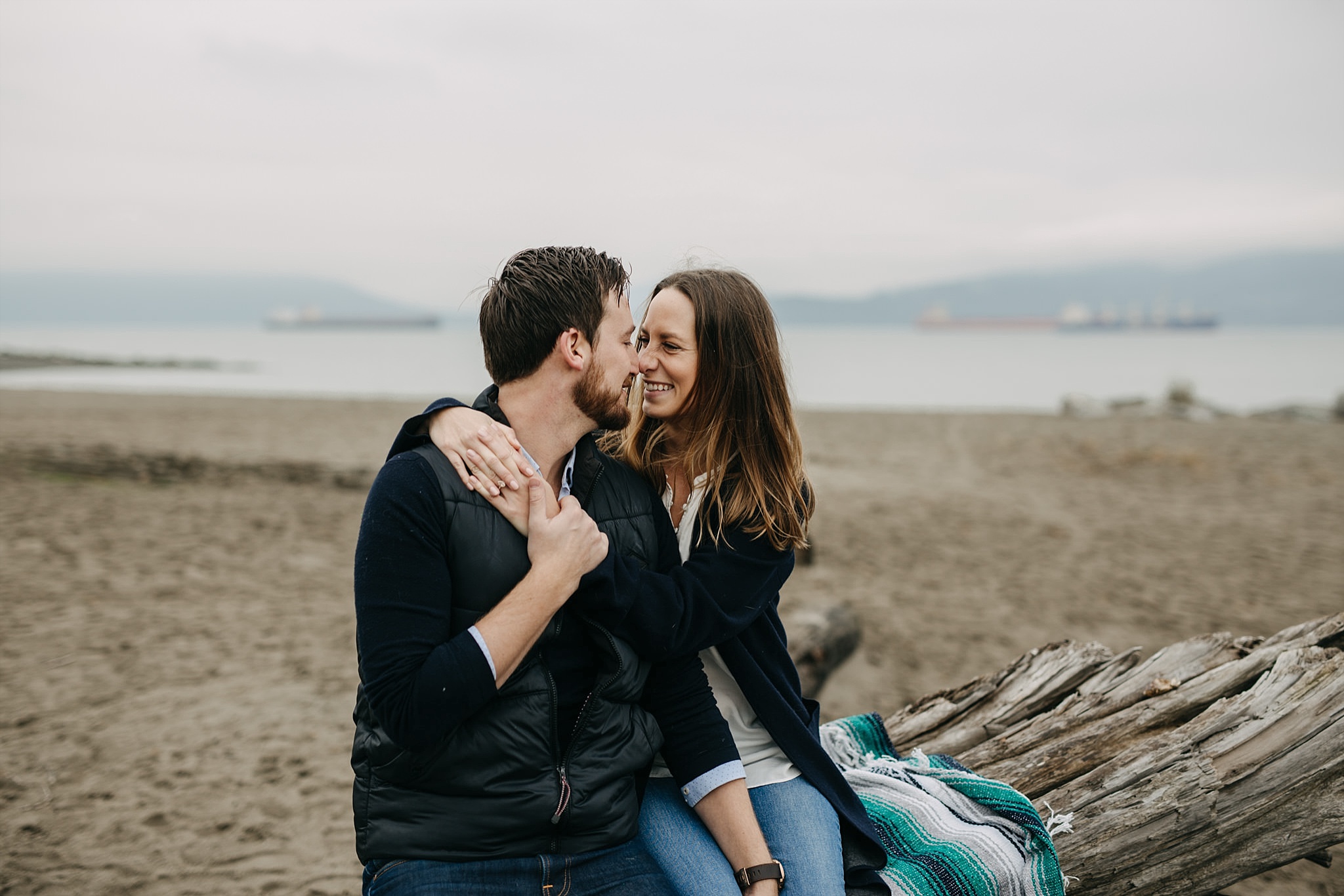 couple arms wrapped around sitting on blanket on log spanish banks engagement
