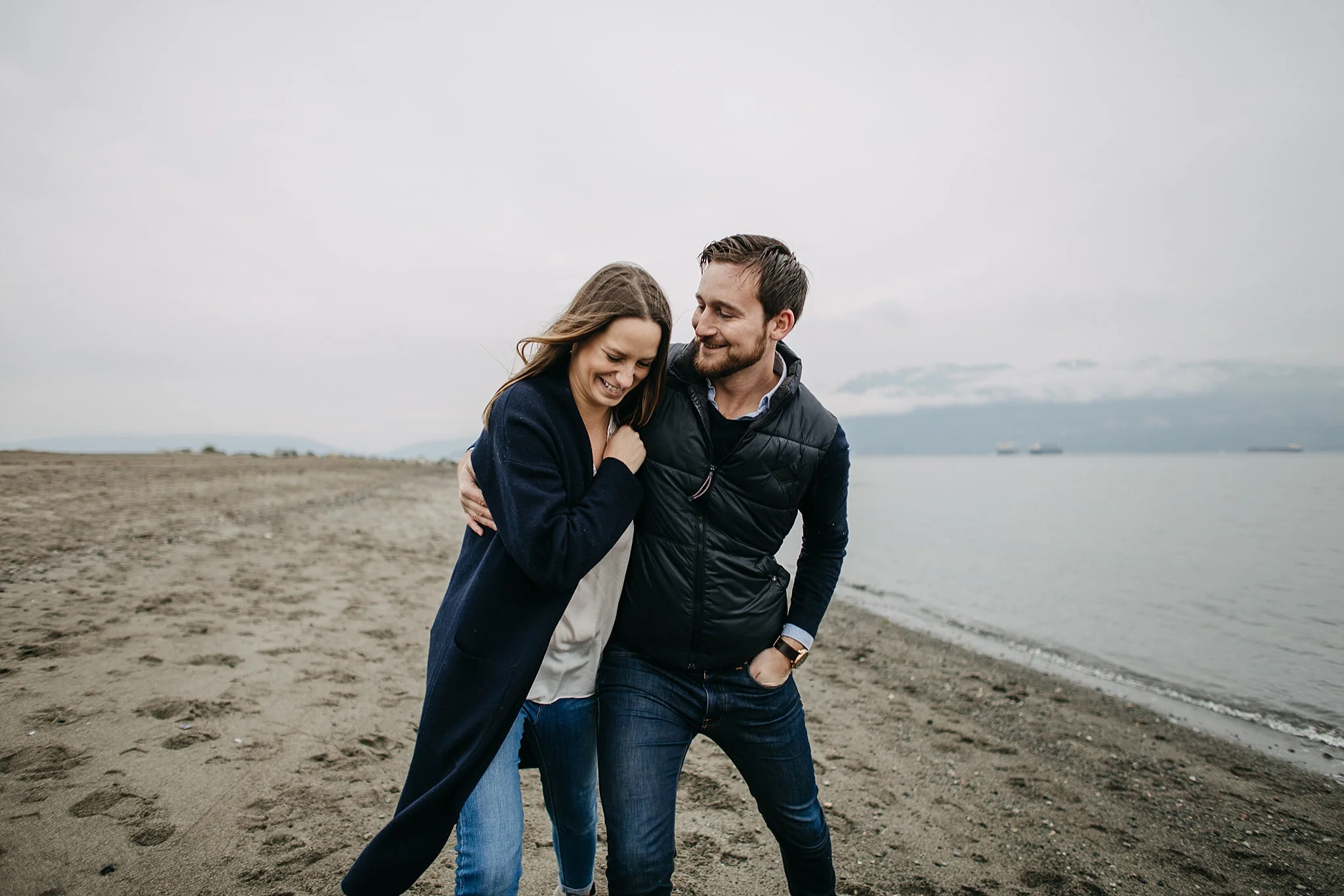guy making fiance laugh walking on beach spanish banks engagement