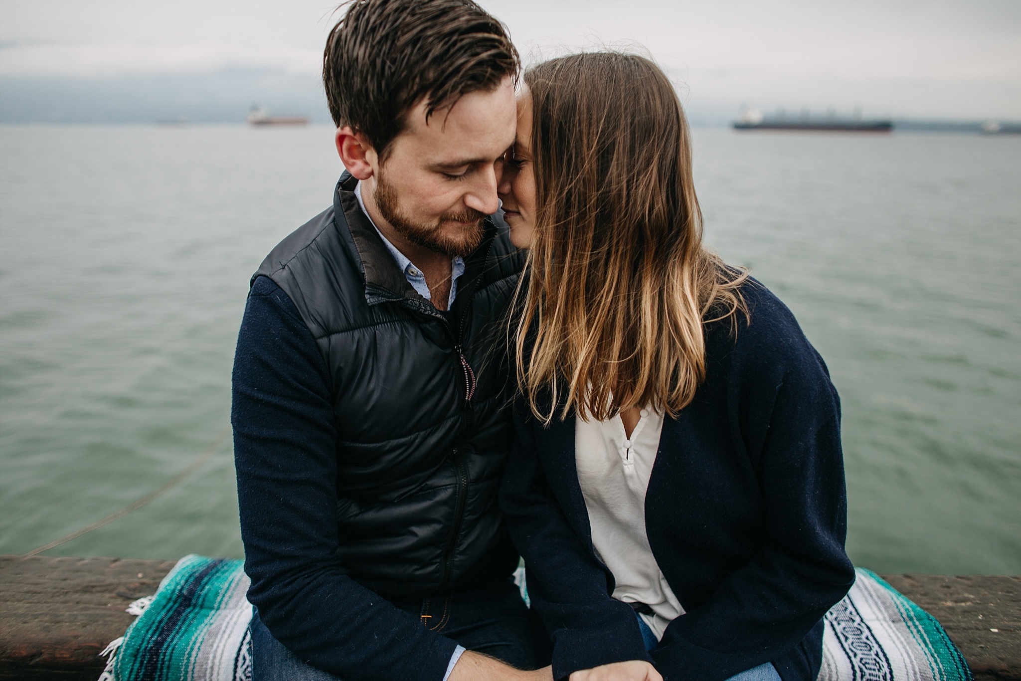 couple snuggling on dock by ocean spanish banks engagement