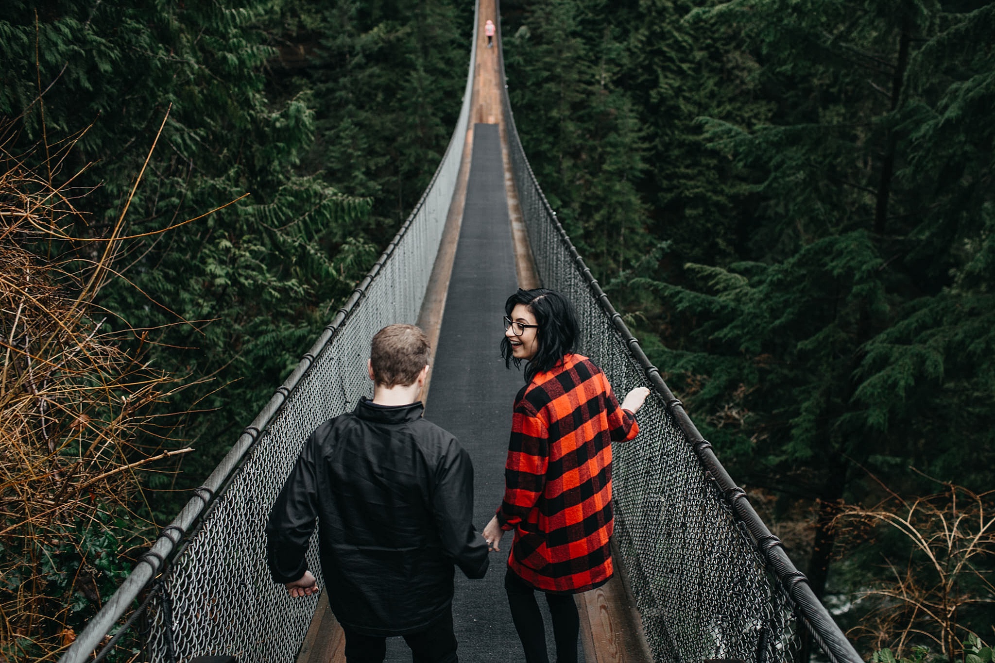 engaged couple walking on capilano suspension bridge holding hands