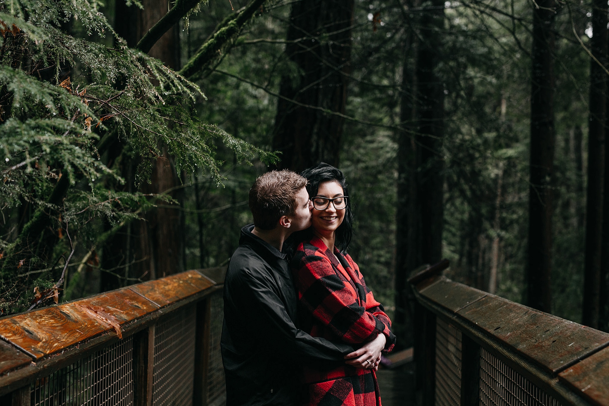 couple kiss on cheek engagement photos capilano suspension bridge north vancouver
