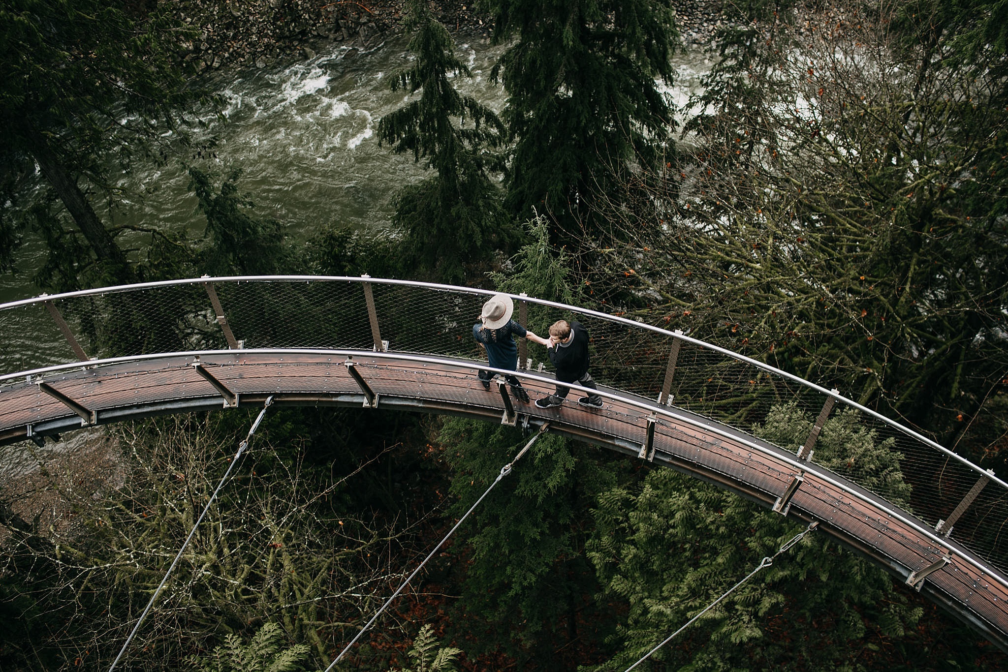couple walking on cliff walk rainy day capilano suspension bridge green trees