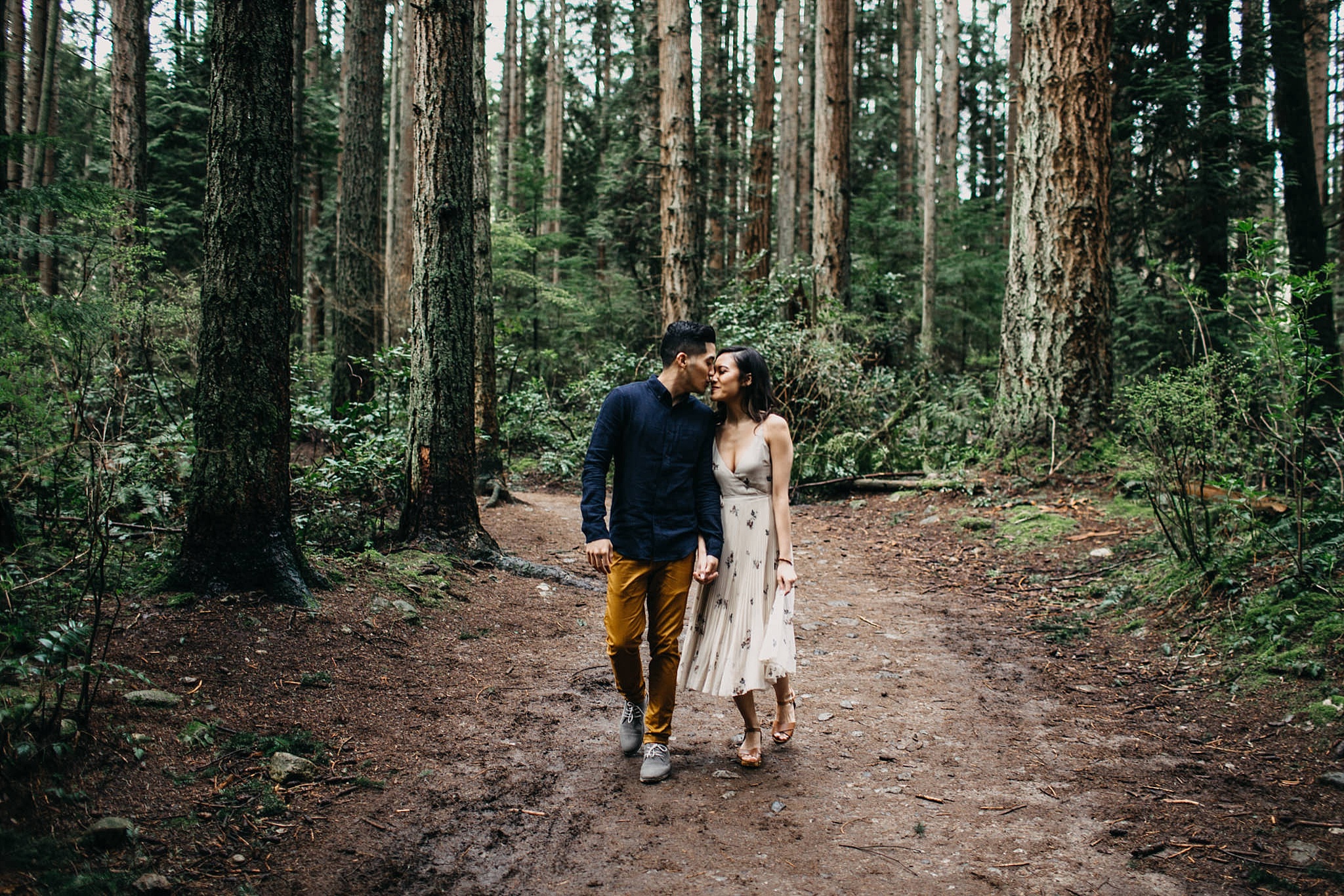 couple walking through forest kissing pacific spirit park engagement