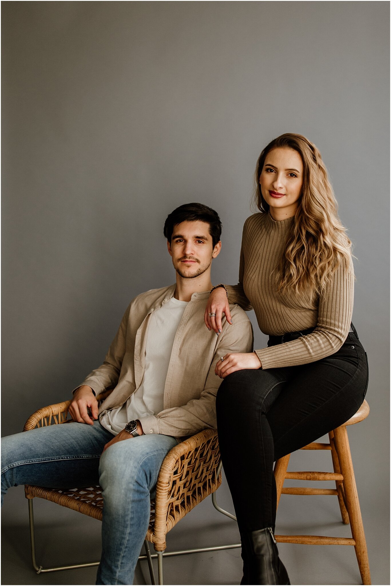 natural light portrait of couple sitting on chairs in front of grey backdrop