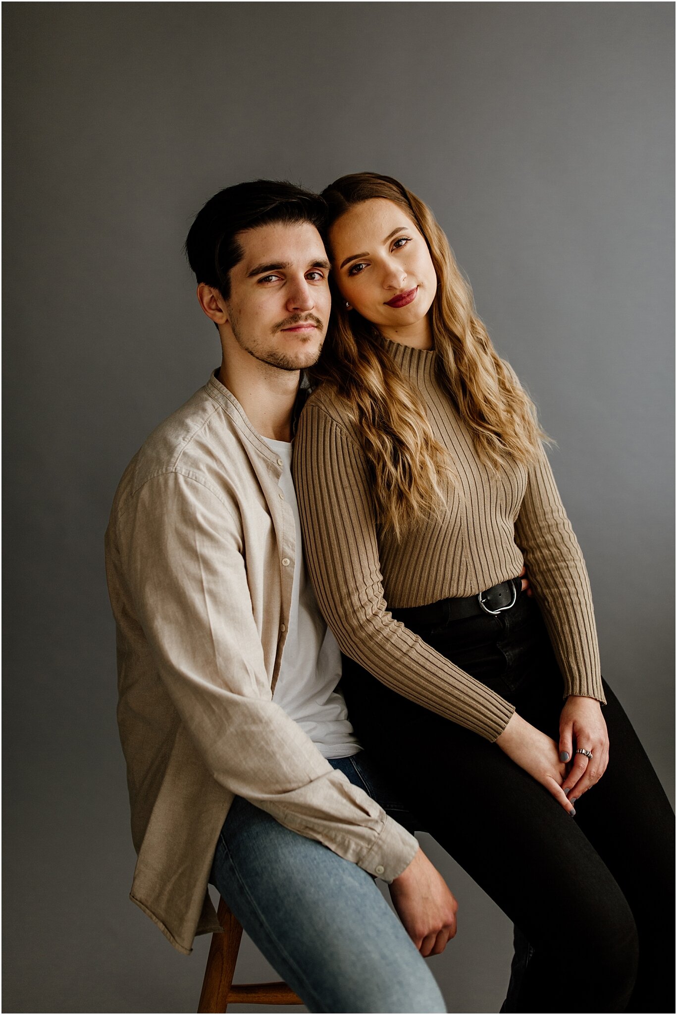 editorial natural light portrait of couple sitting on stool with grey backdrop