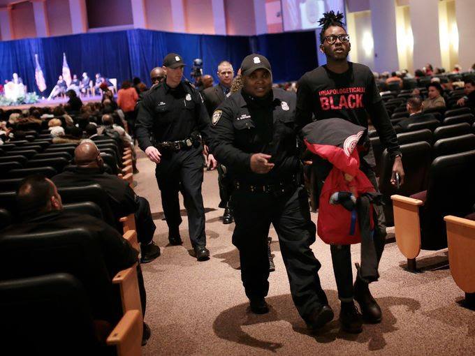 Dakarai Carter being escorted out of the State of the City address after disruption. Photo Credit: Julia Cuneo