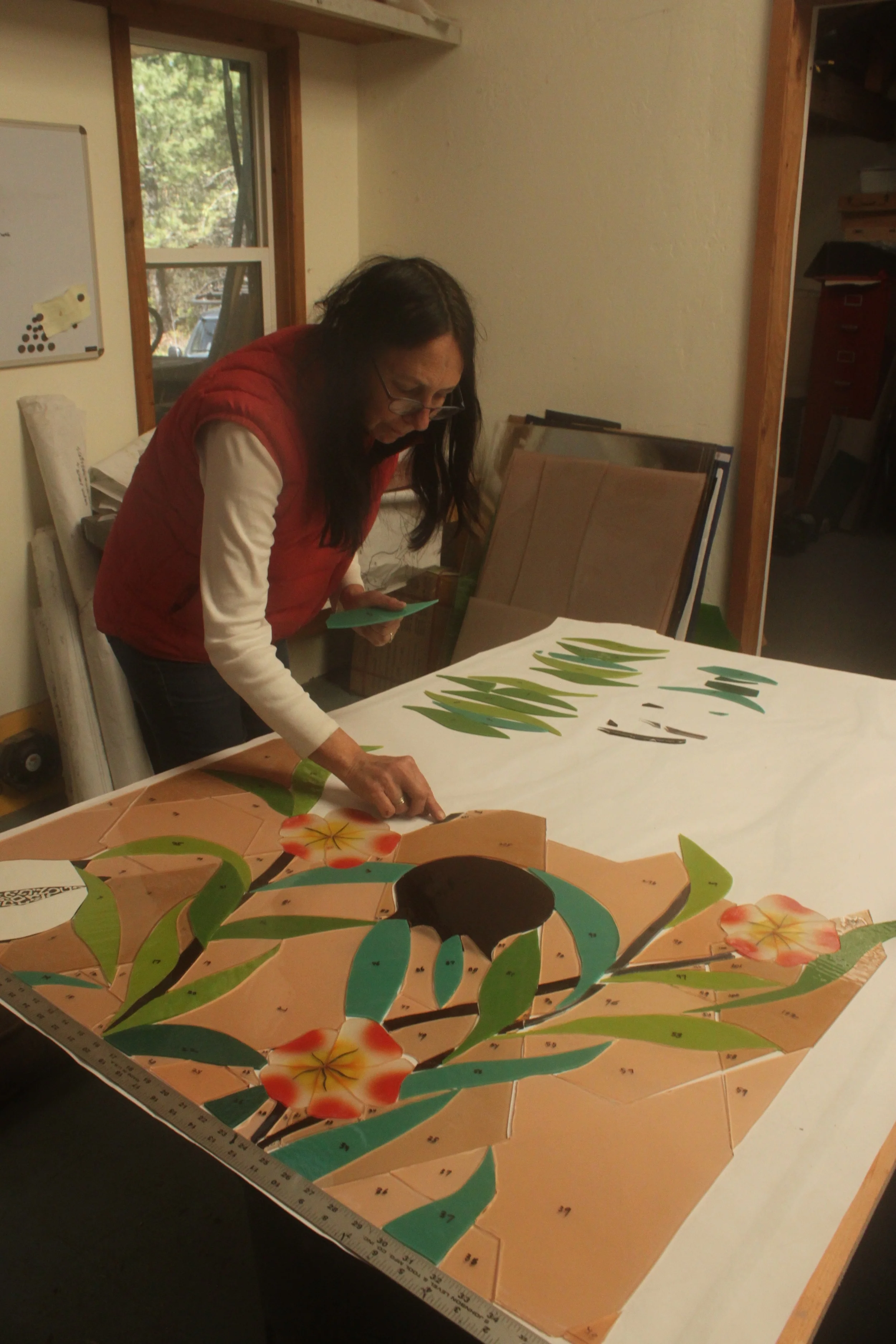 Michelle places completed pieces on the lay out table as she continues cutting glass.