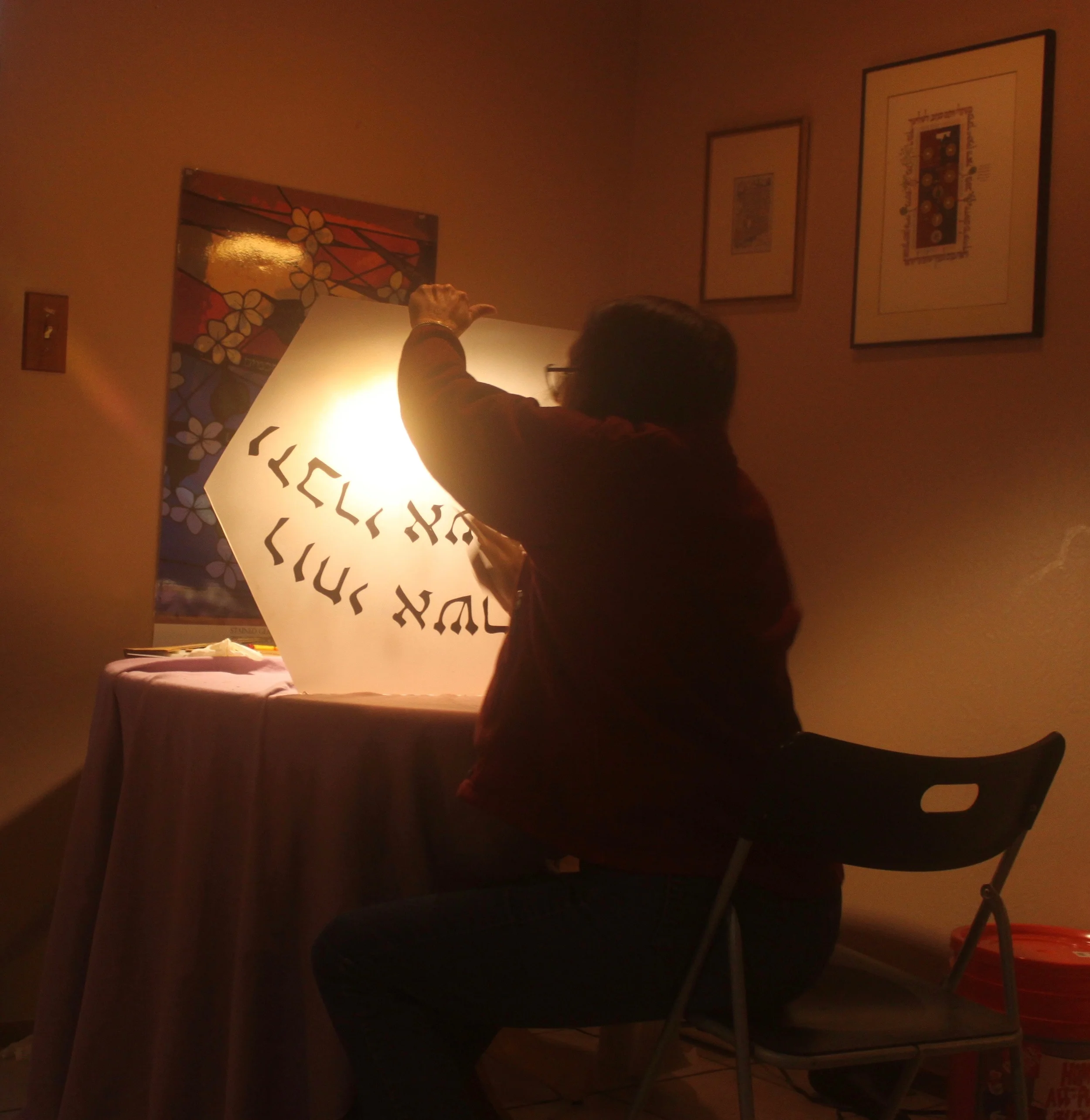 Michelle examines the painted piece for flaws and light spots before releasing the piece to the kiln for firing.