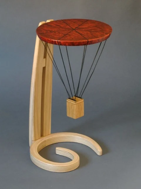 A small occasional table presented to a young man (initials G.H.) in recognition of his being awarded a hot air balloon pilot's license. The 'gondola' will hold a small keepsake. Ash, dyed curly maple, ebony. 