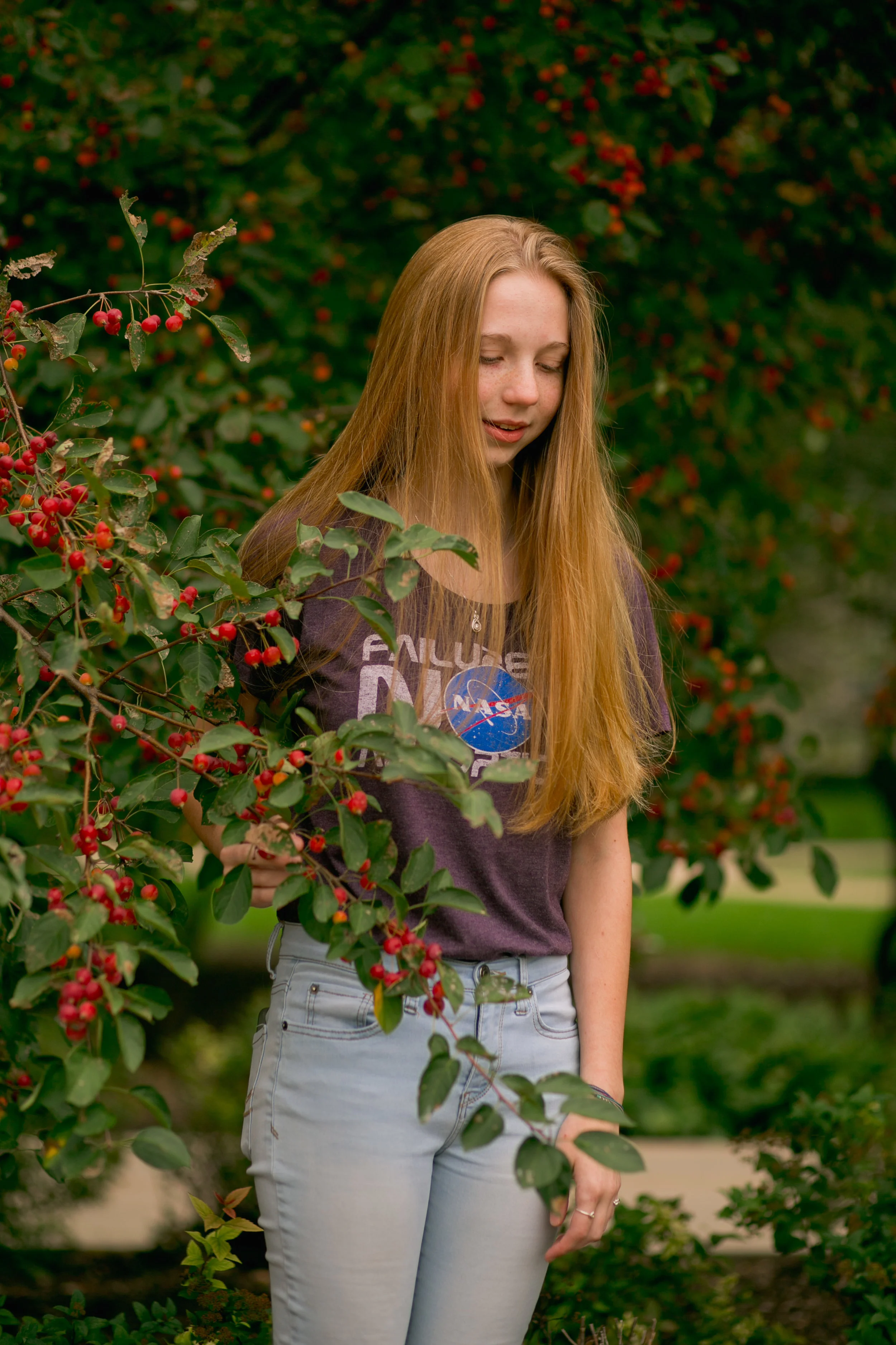 senior girl wearing nasa tshirt and light blue jeans standing in low tree