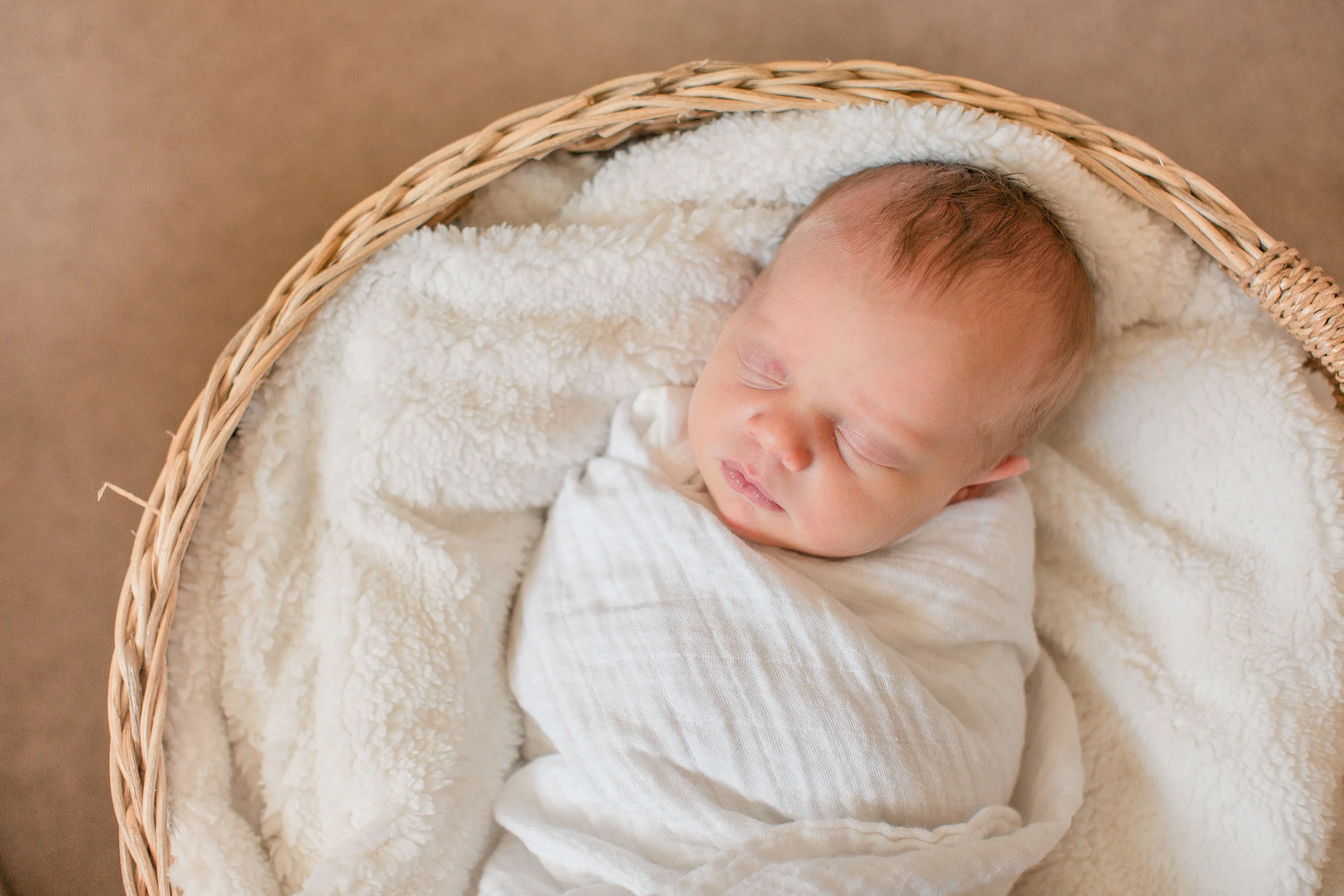sweet newborn girl sleeping in swaddle inside basket with white blanket