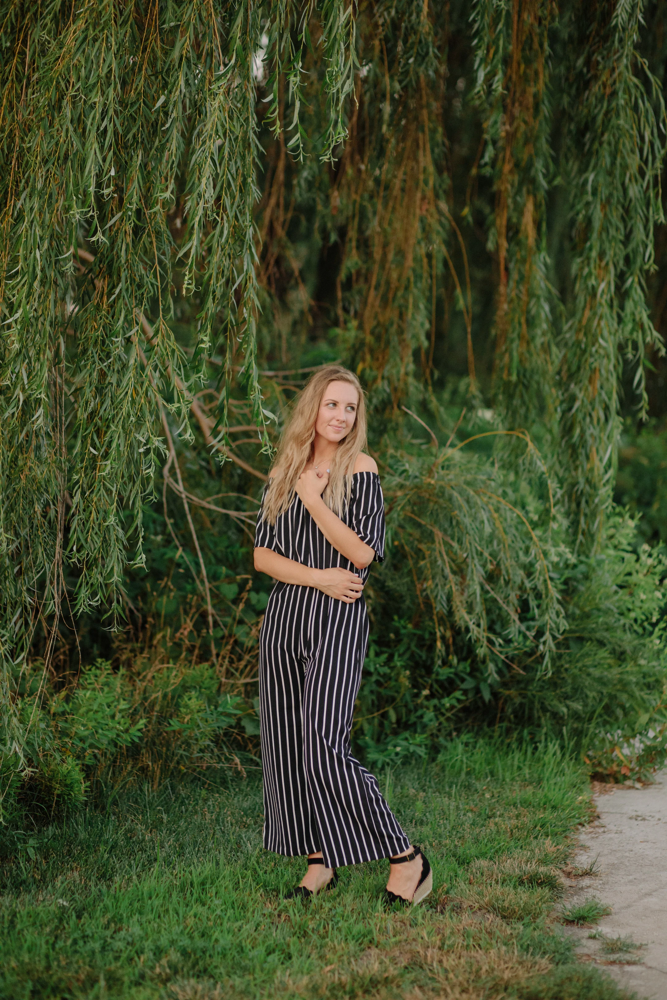 girl wearing striped jumpsuit in front of weeping willow tree senior photos des moines