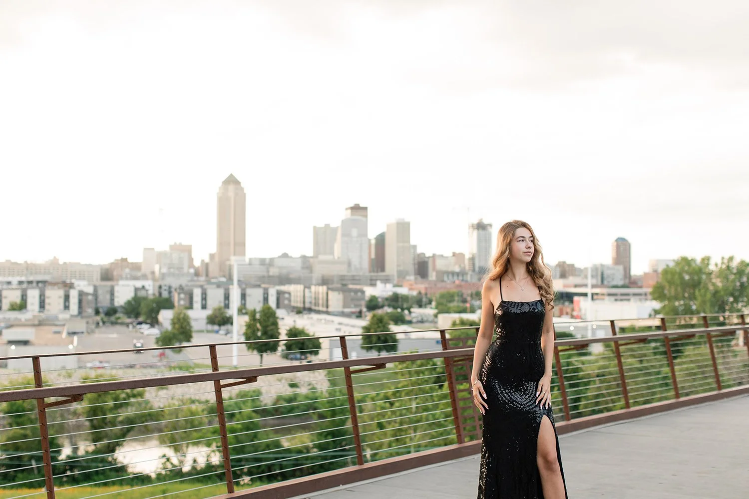 girl in formal dress for senior photos standing with des moines skyline behind her