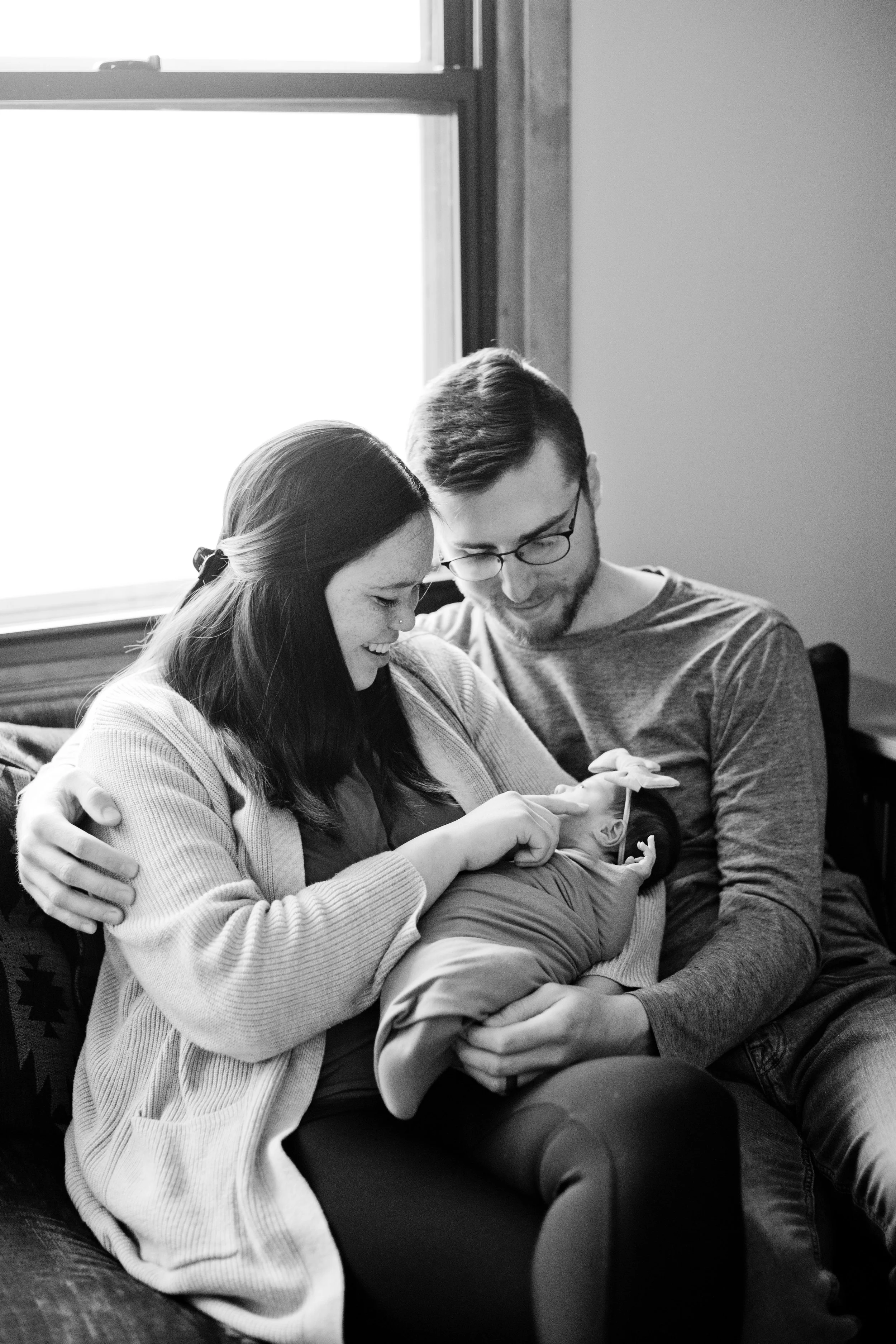 parents holding and smiling at newborn baby on couch