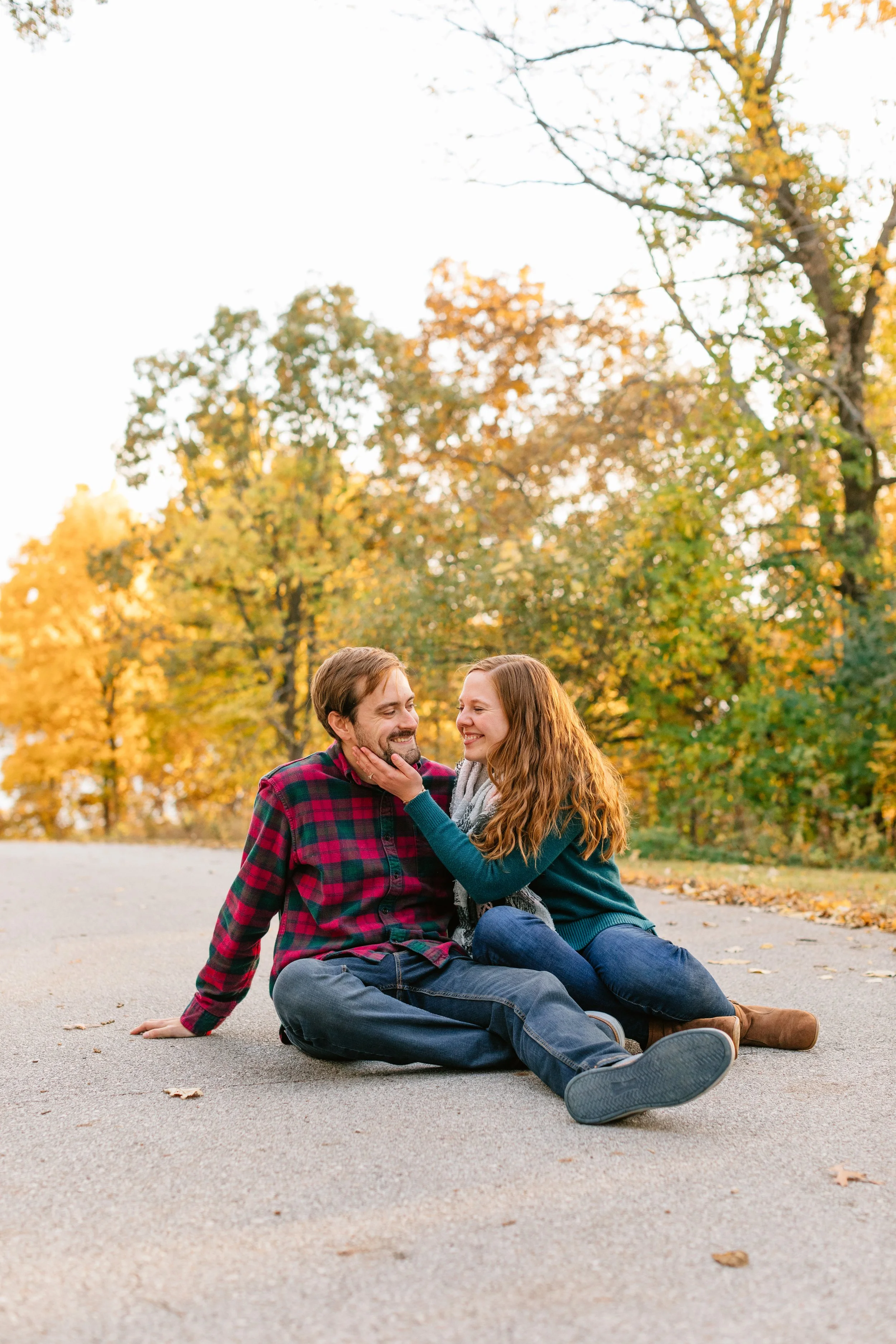 couple sitting on path near colorful trees in fall