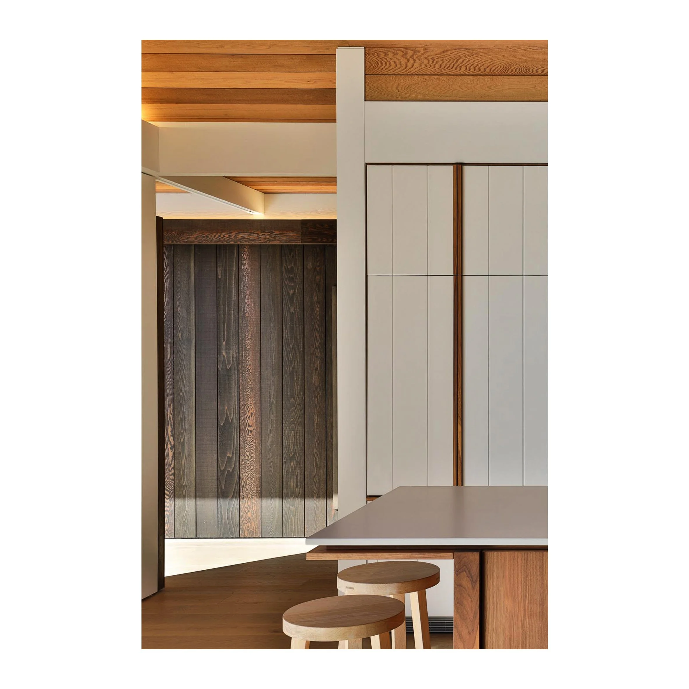 Interior view of a modern kitchen with wooden cabinets, white paneling, and a wooden ceiling, featuring a partial view of a countertop and two wooden stools.