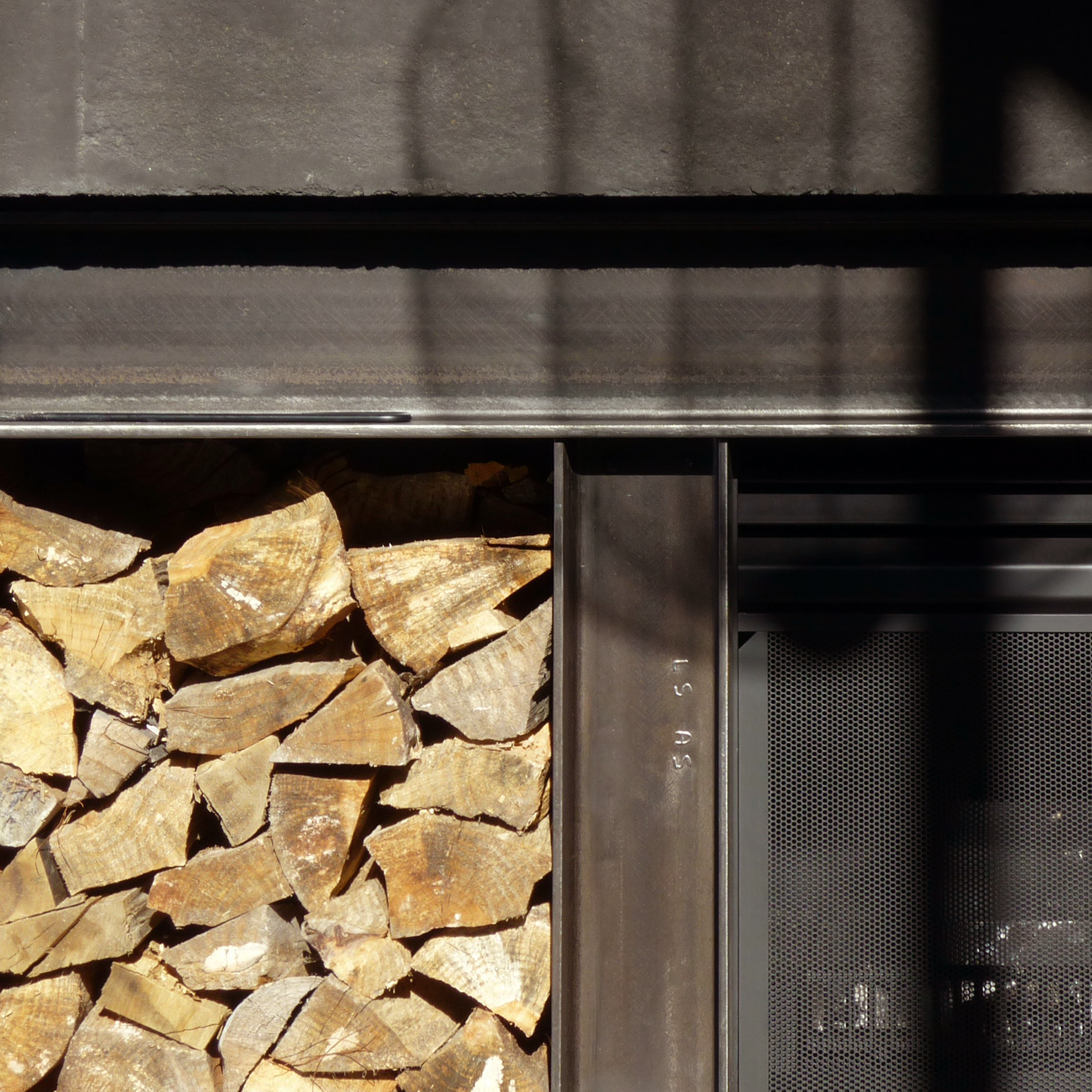 Stacked firewood next to a metal storage container with a perforated panel.